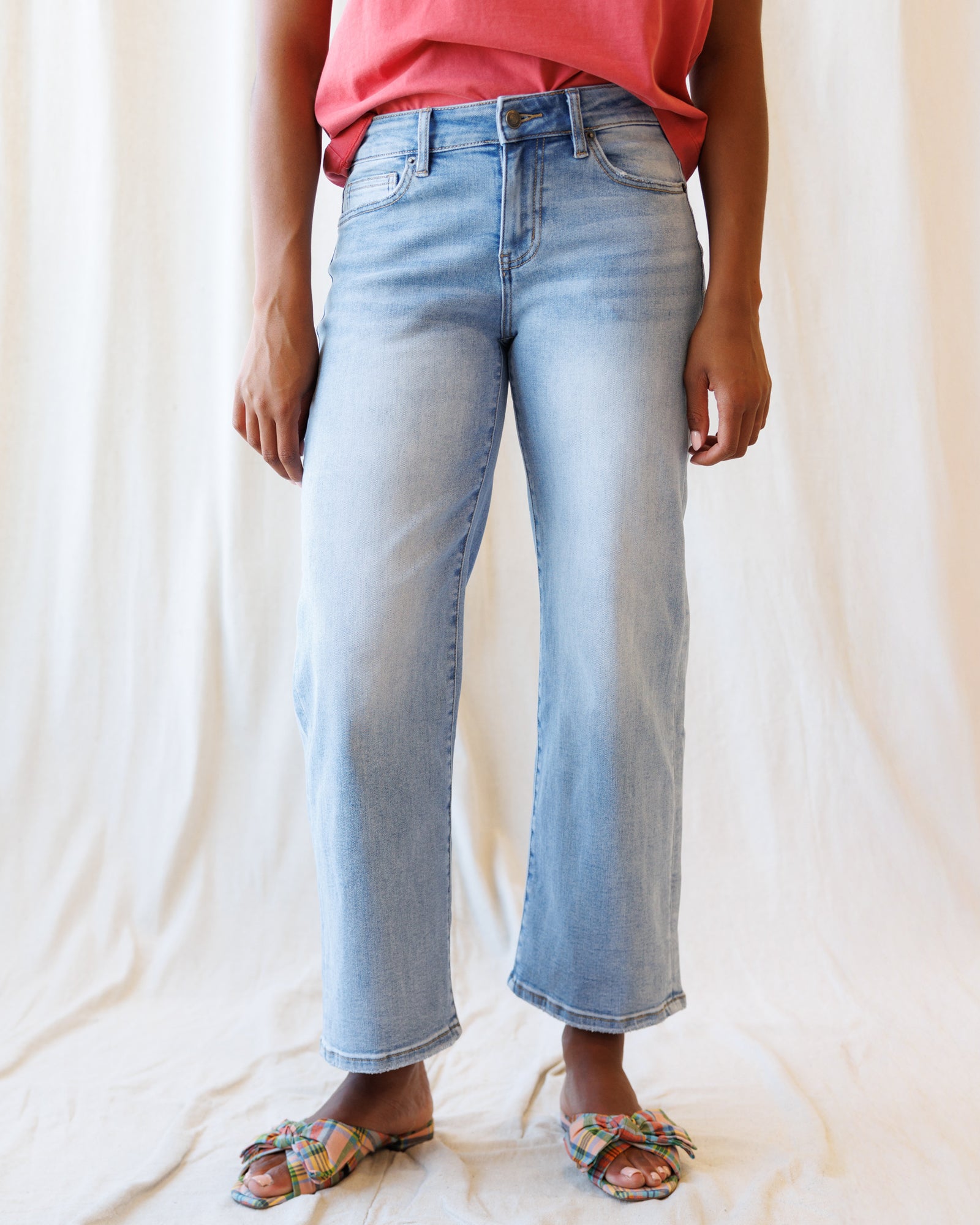 Person wearing light blue jeans and a pink top on a plain background
