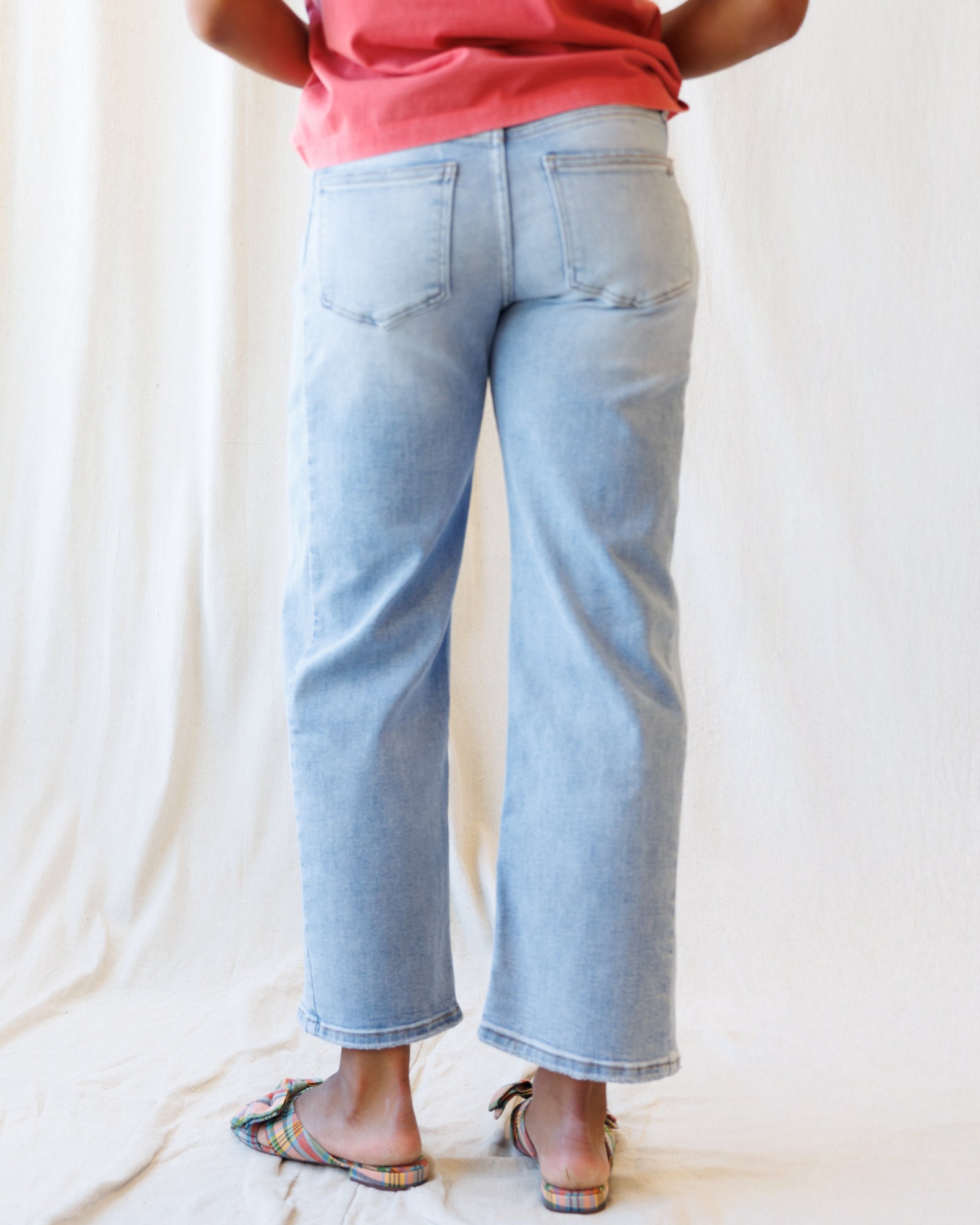 Person wearing light blue jeans and a pink top on a plain background