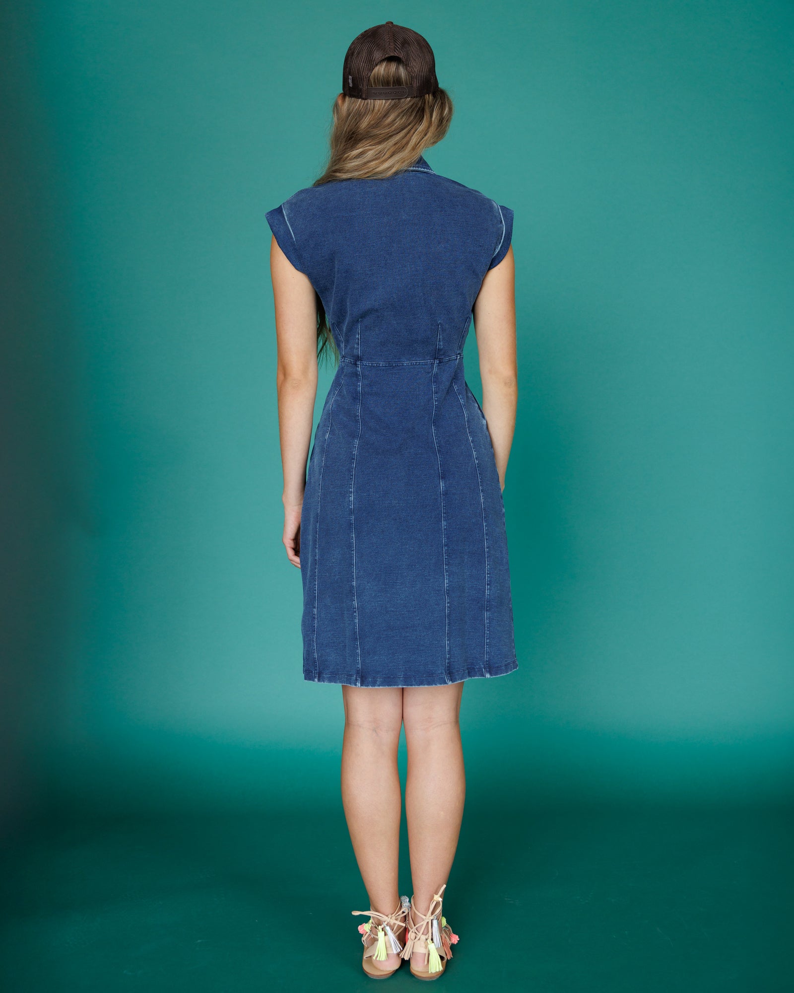Woman wearing a blue denim dress against a teal background