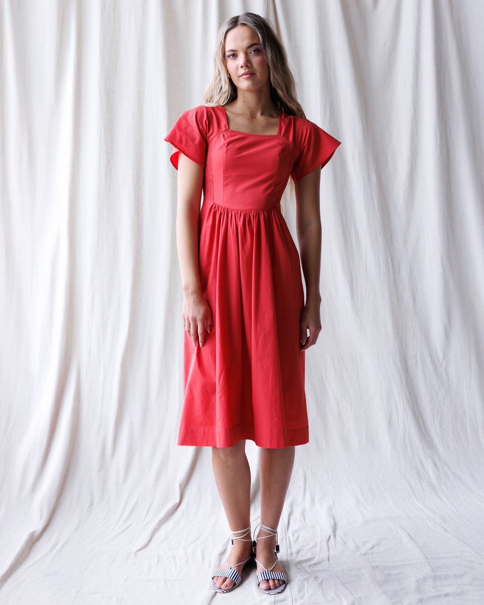 Woman wearing a red dress against a white curtain background