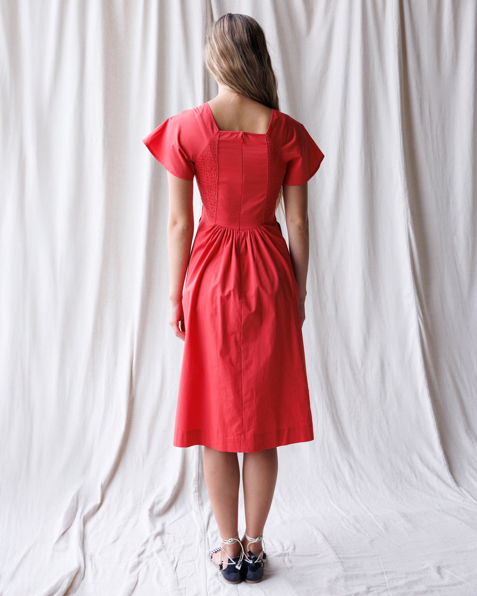 Woman wearing a red dress standing against a white curtain