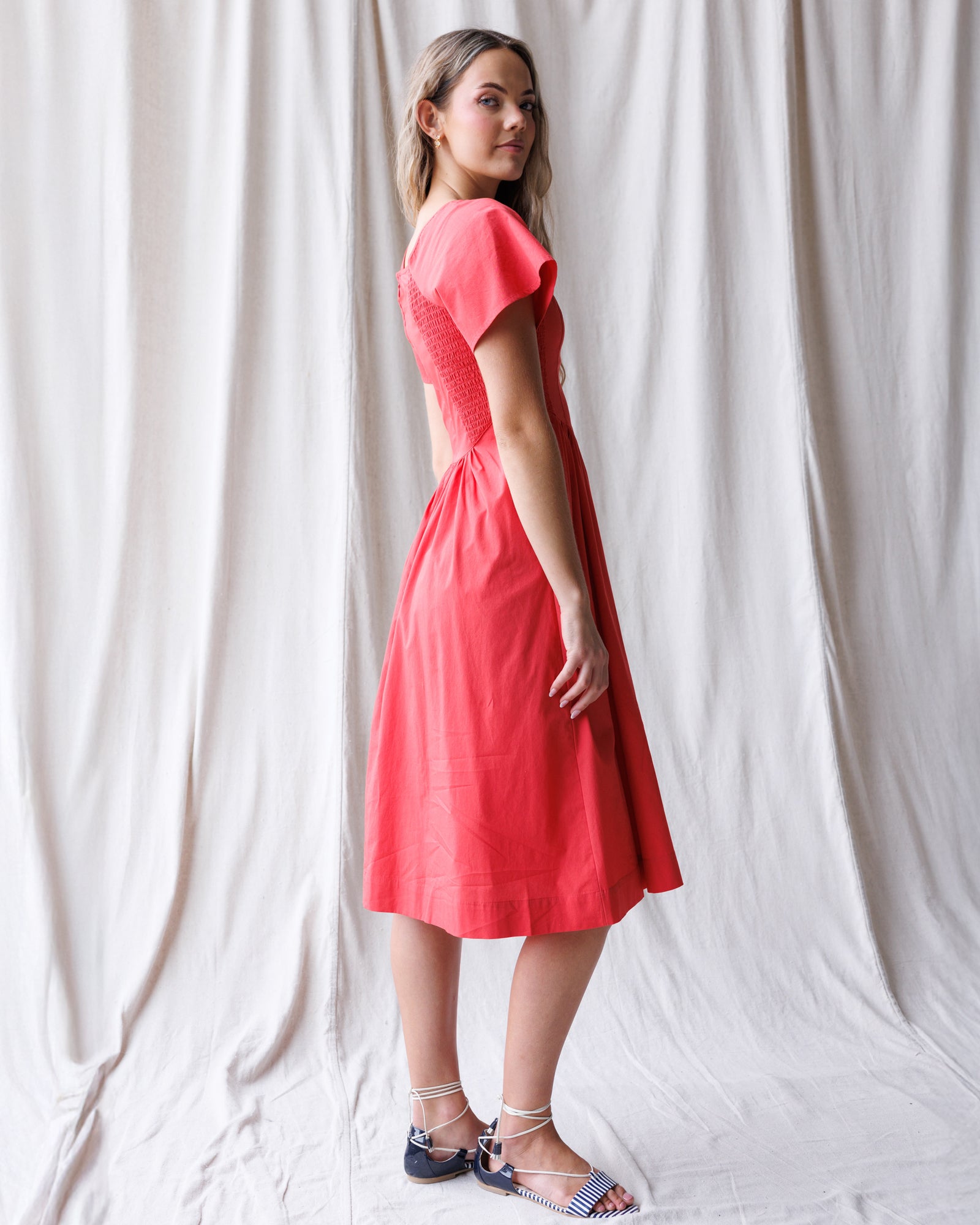 Woman wearing a red dress standing against a white curtain