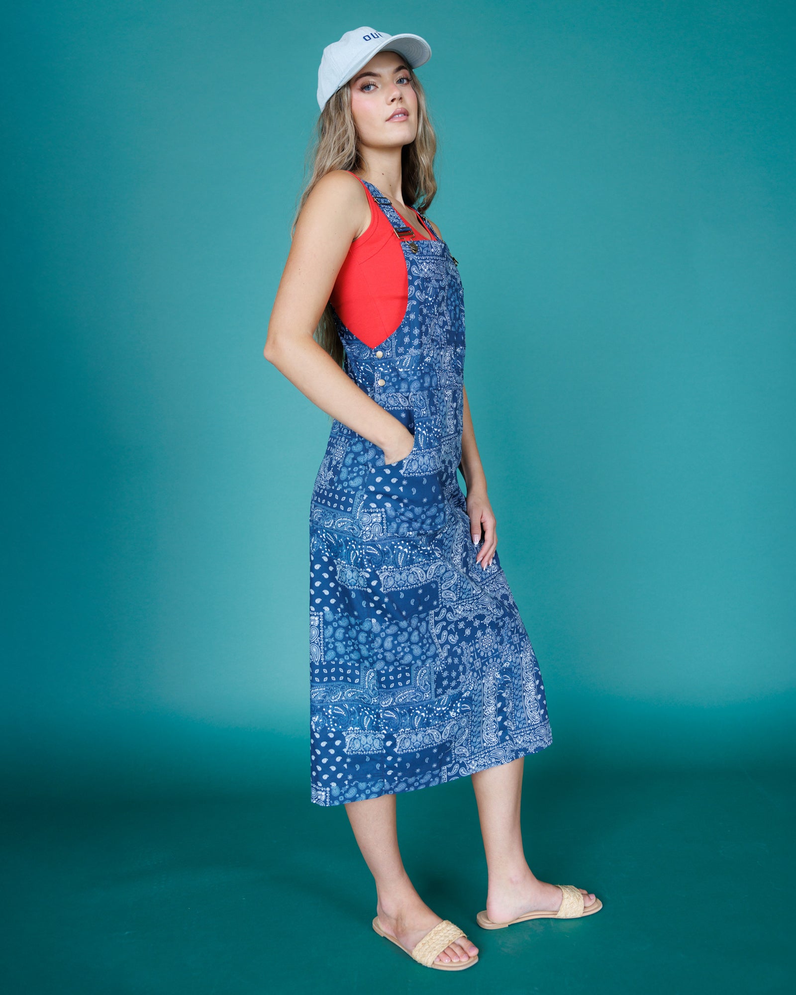 Woman wearing a blue patterned dress over a red tank top against a teal background