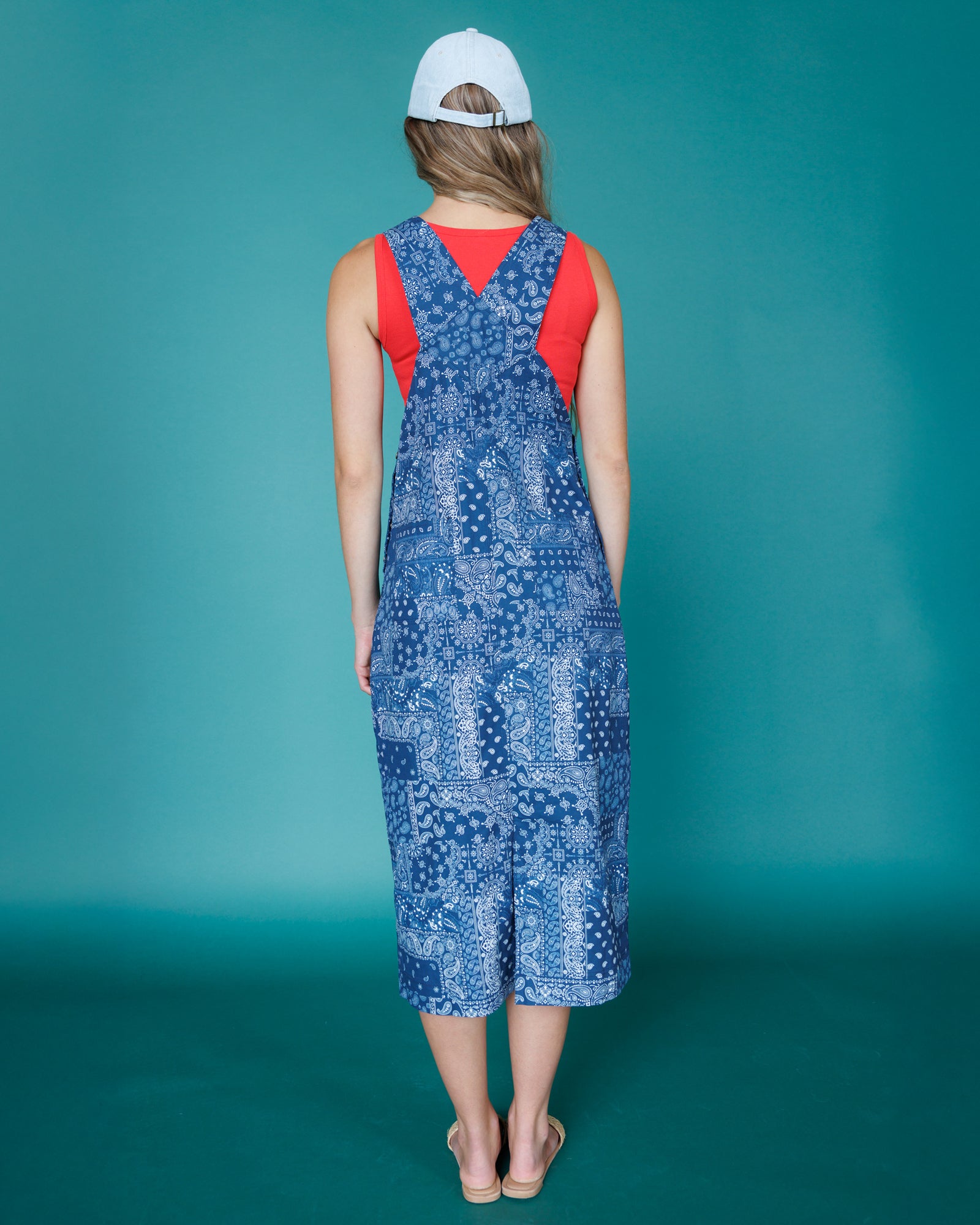 Woman wearing a blue patterned dress with a red top against a teal background