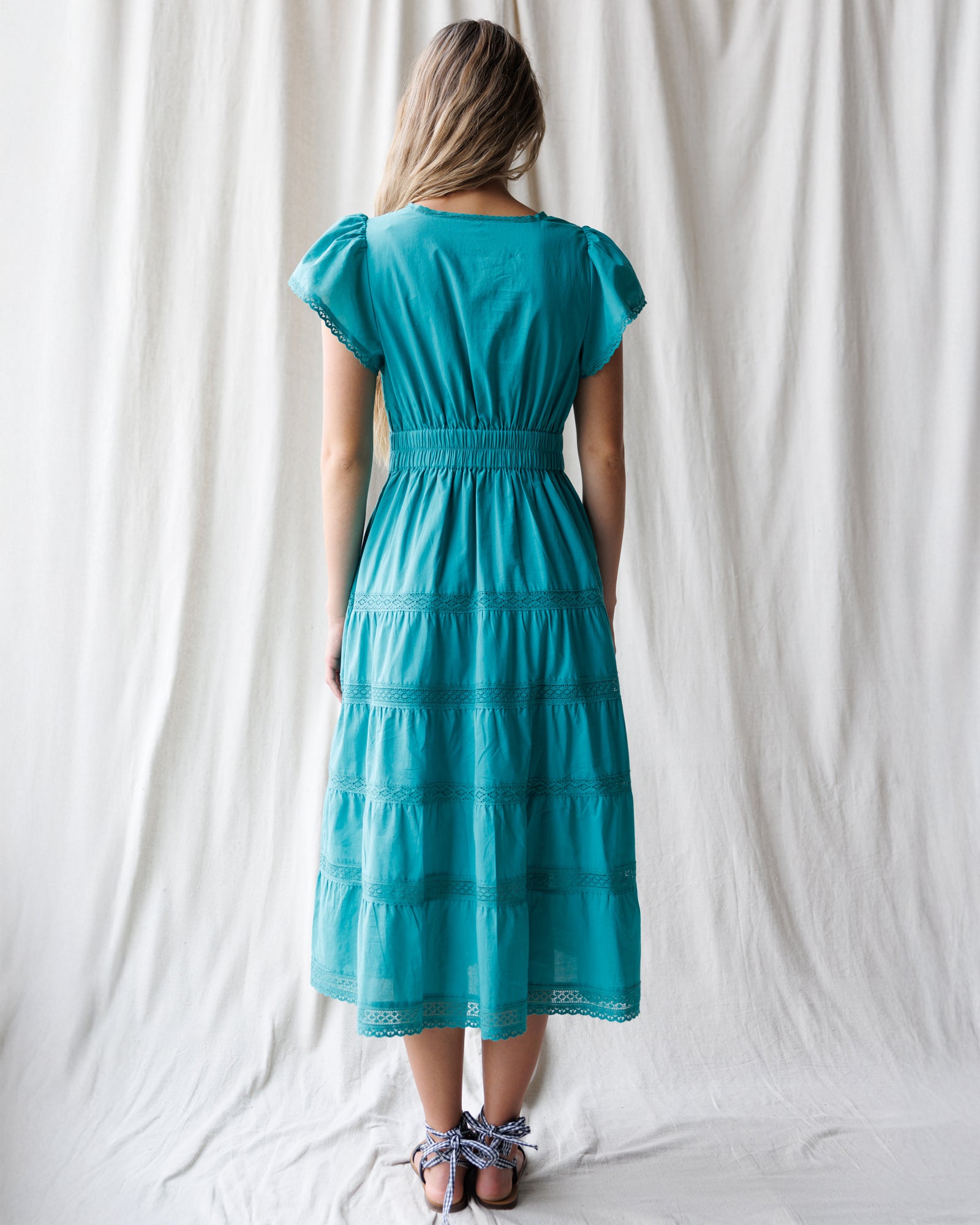 Woman wearing a teal dress standing against a white curtain