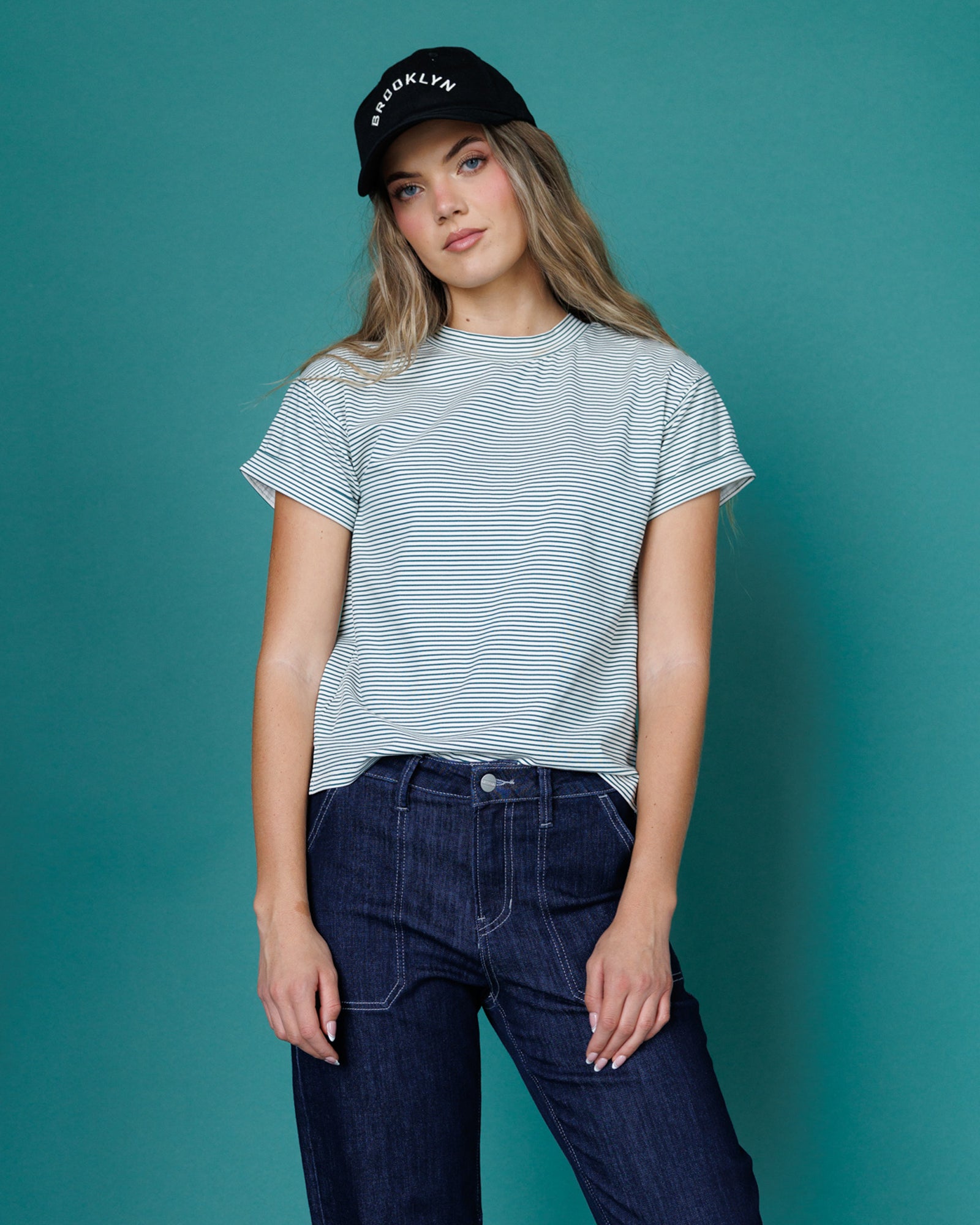 Woman wearing a striped t-shirt and dark jeans against a teal background