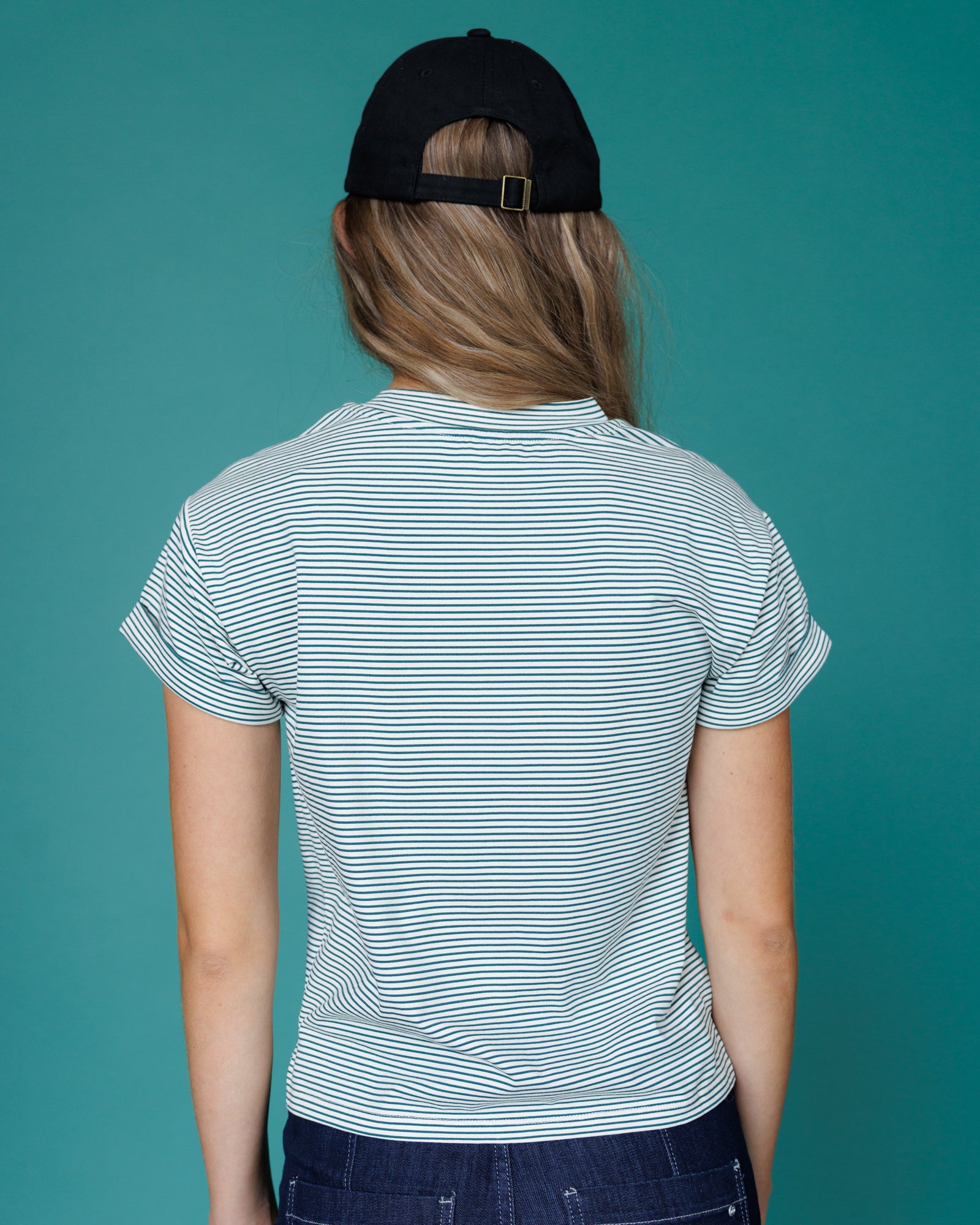 Person wearing a striped t-shirt and black cap on a teal background