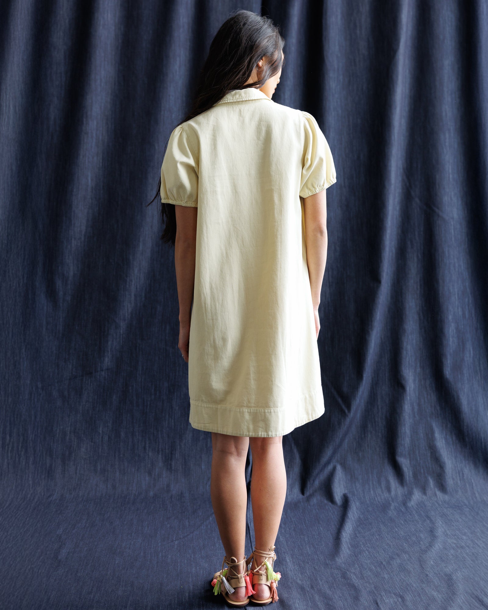 Person wearing a light-colored dress against a dark blue curtain