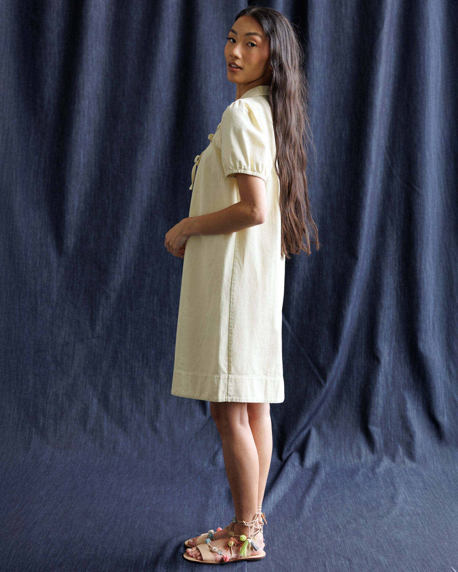 Woman wearing a light-colored dress against a dark blue curtain