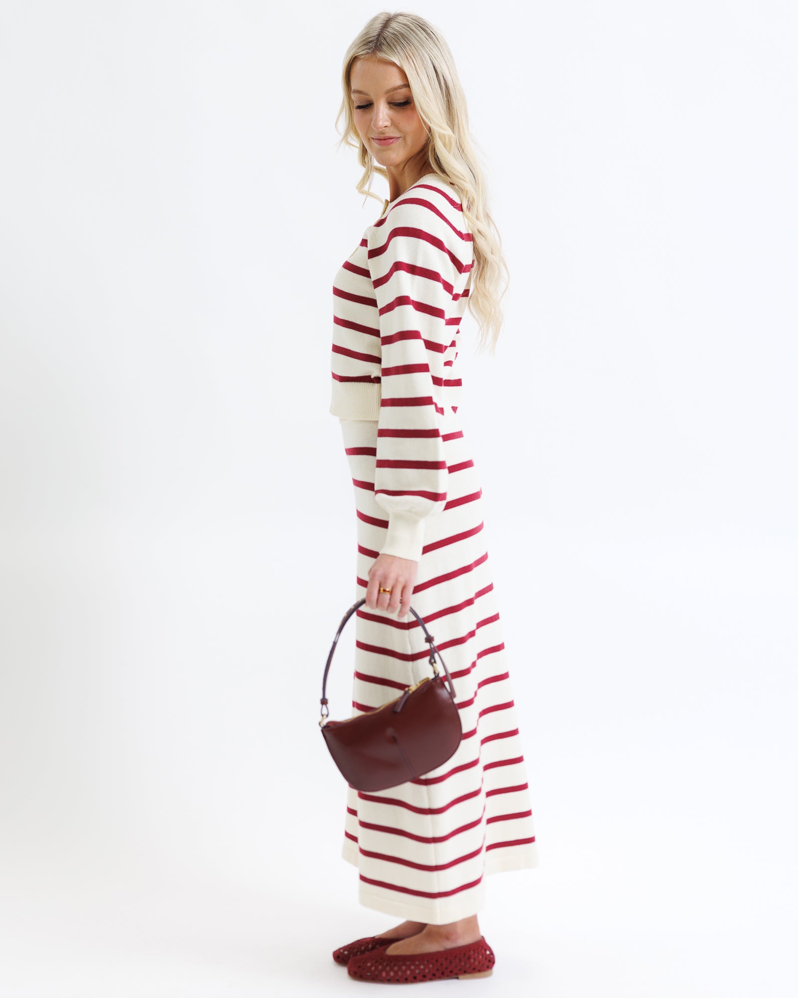 Woman wearing a red and white striped dress holding a brown handbag on a white background