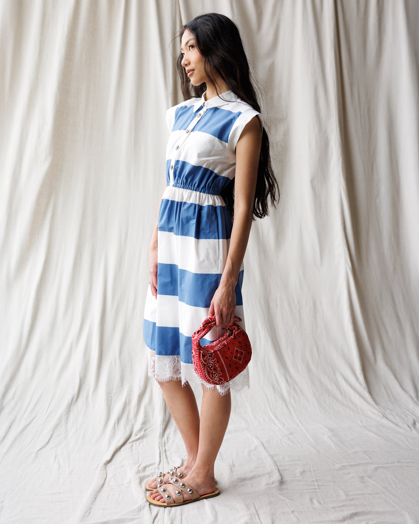 Woman wearing a blue and white striped dress holding a red handbag against a plain background