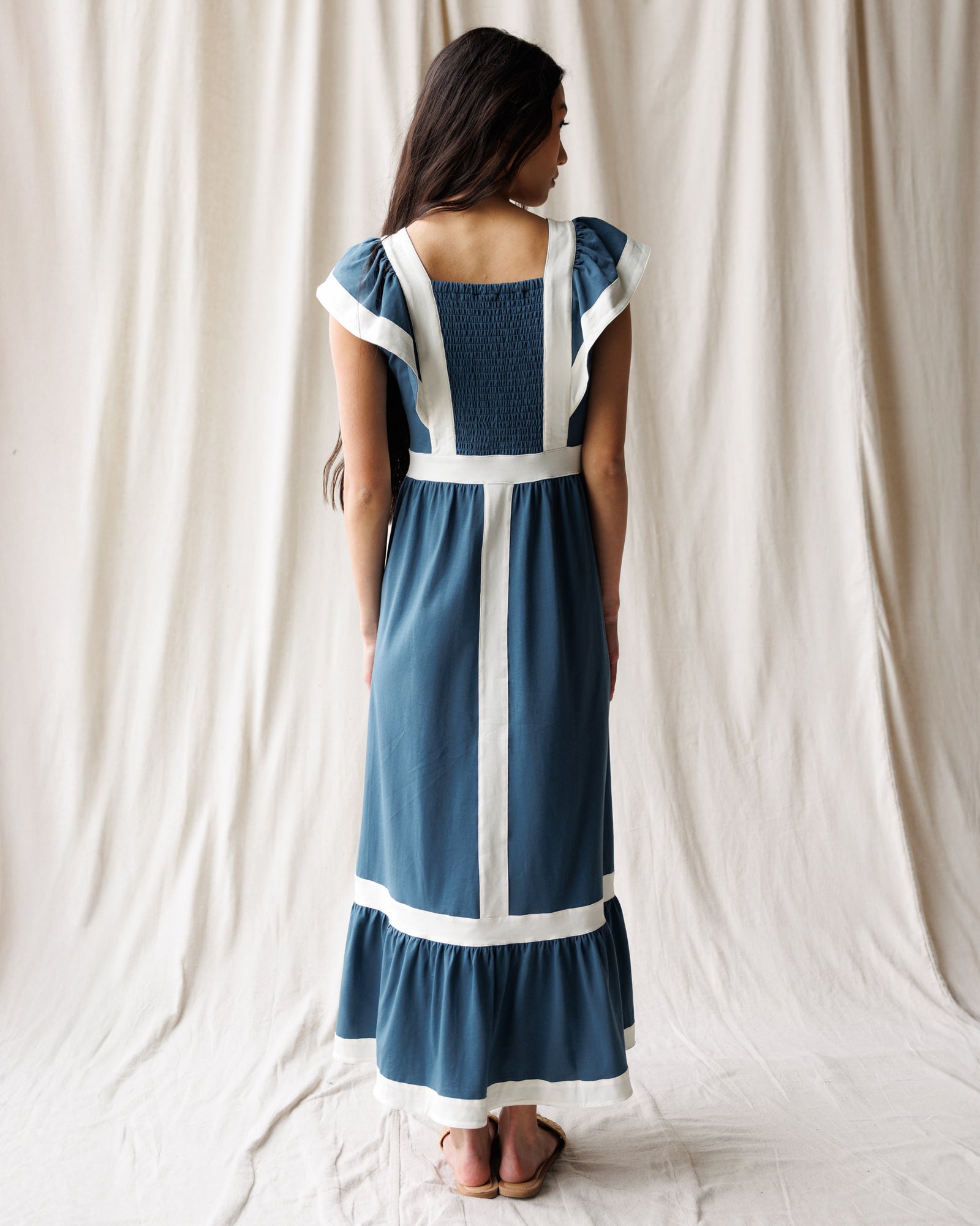 Woman wearing a blue dress with white accents against a white curtain background