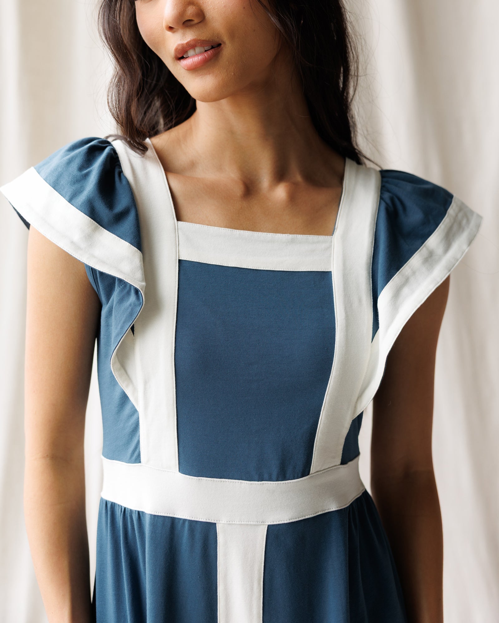 Woman wearing a blue dress with white accents against a neutral background