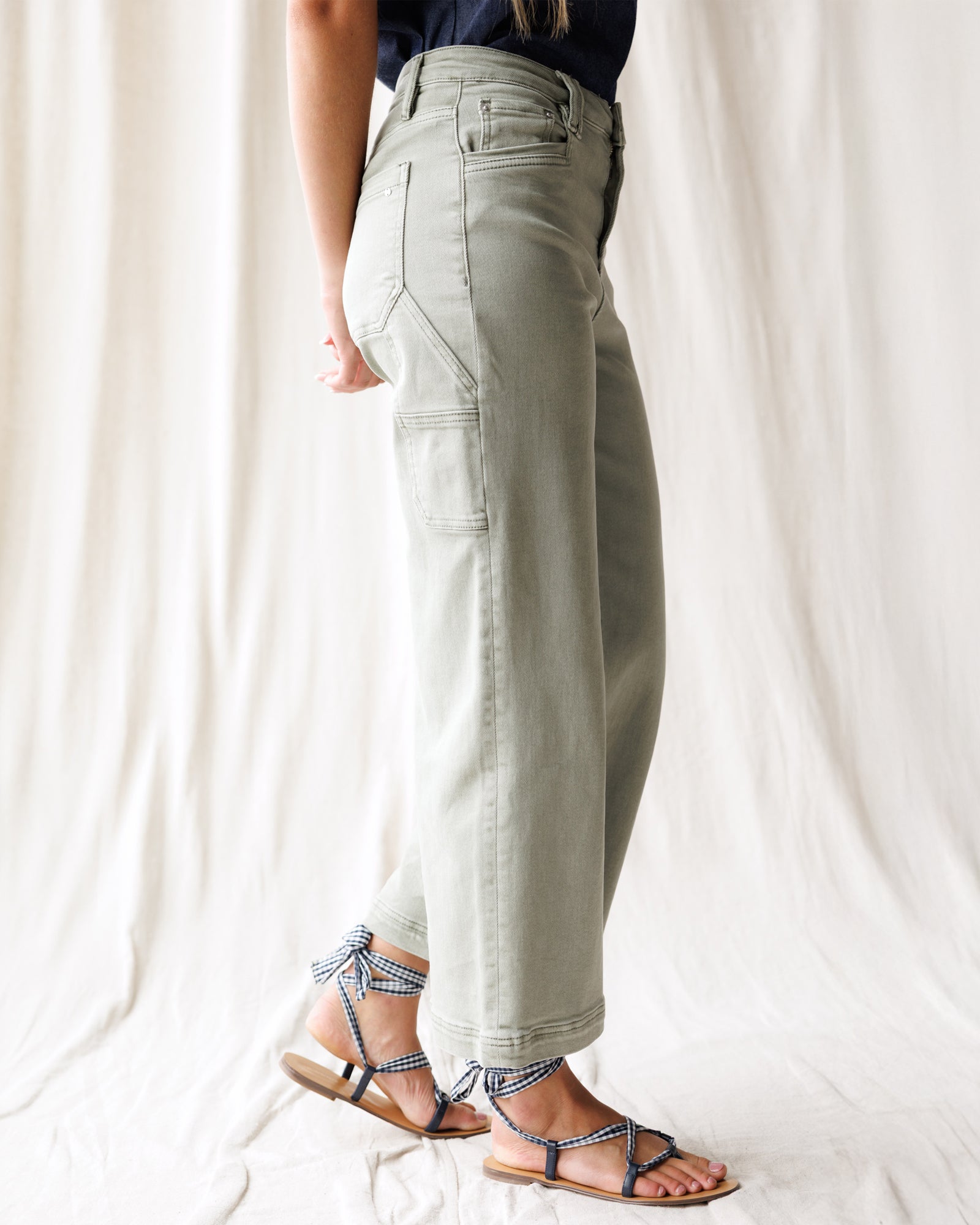 Person wearing light green pants and strappy sandals on a white background