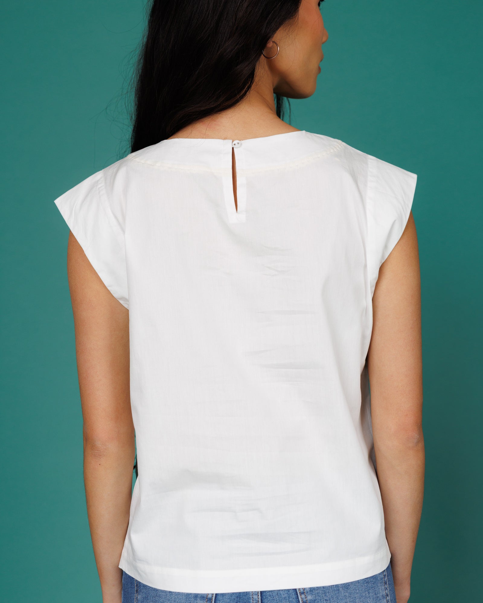 White sleeveless top worn by a person on a teal background