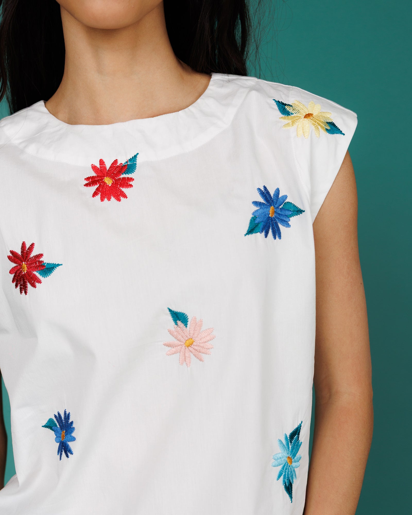 White sleeveless top with colorful floral embroidery on a green background