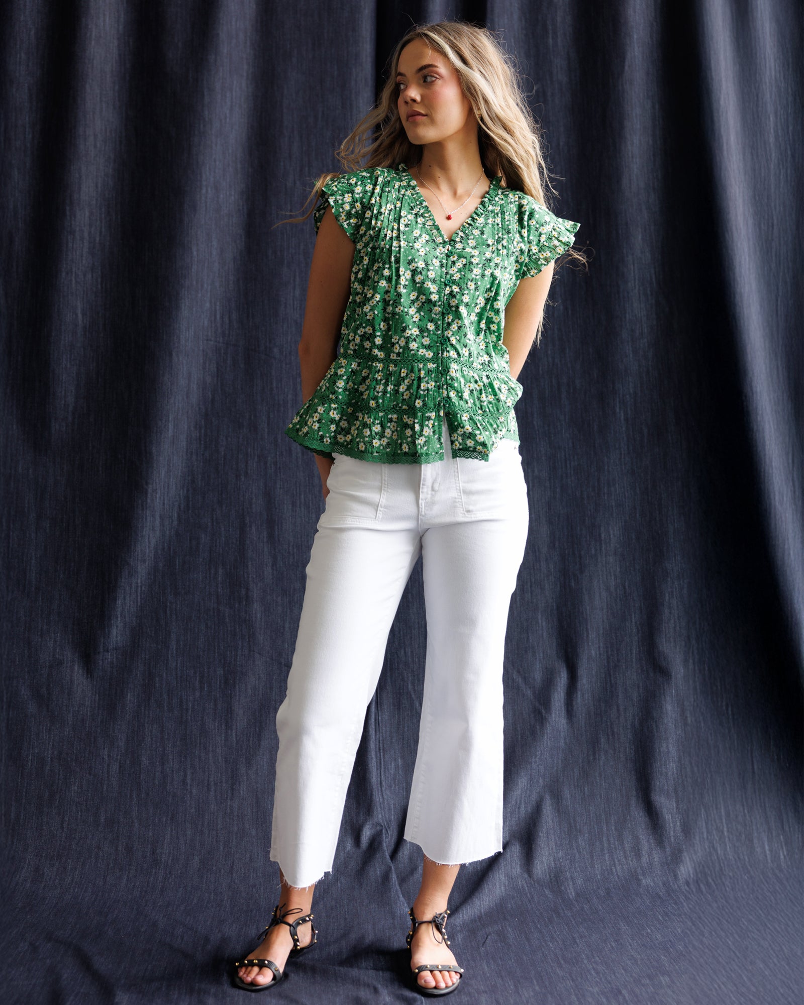 Woman wearing a green floral top and white pants against a dark background