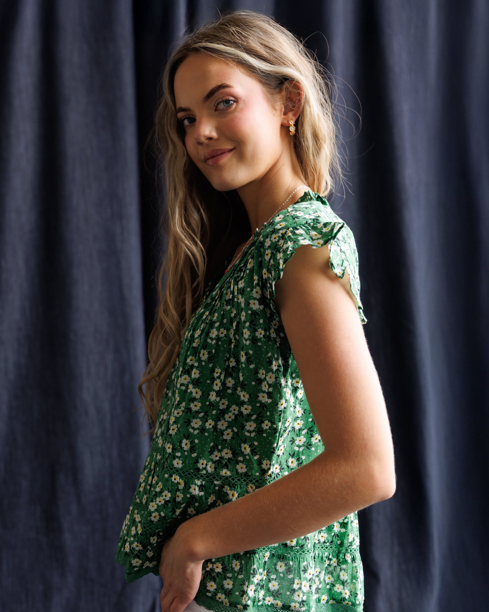 Woman wearing a green floral dress against a dark blue curtain
