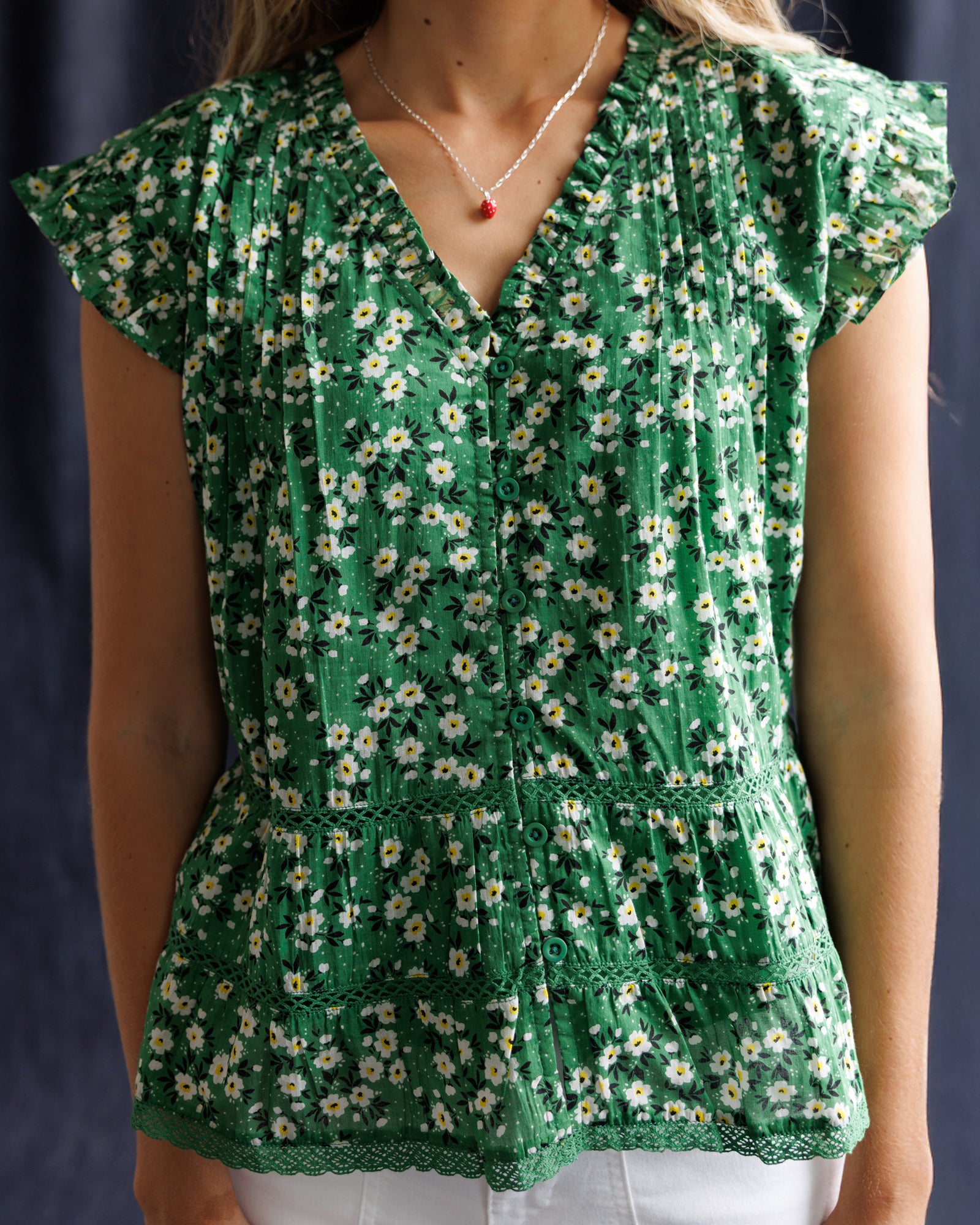 Green floral blouse worn by a person against a dark background