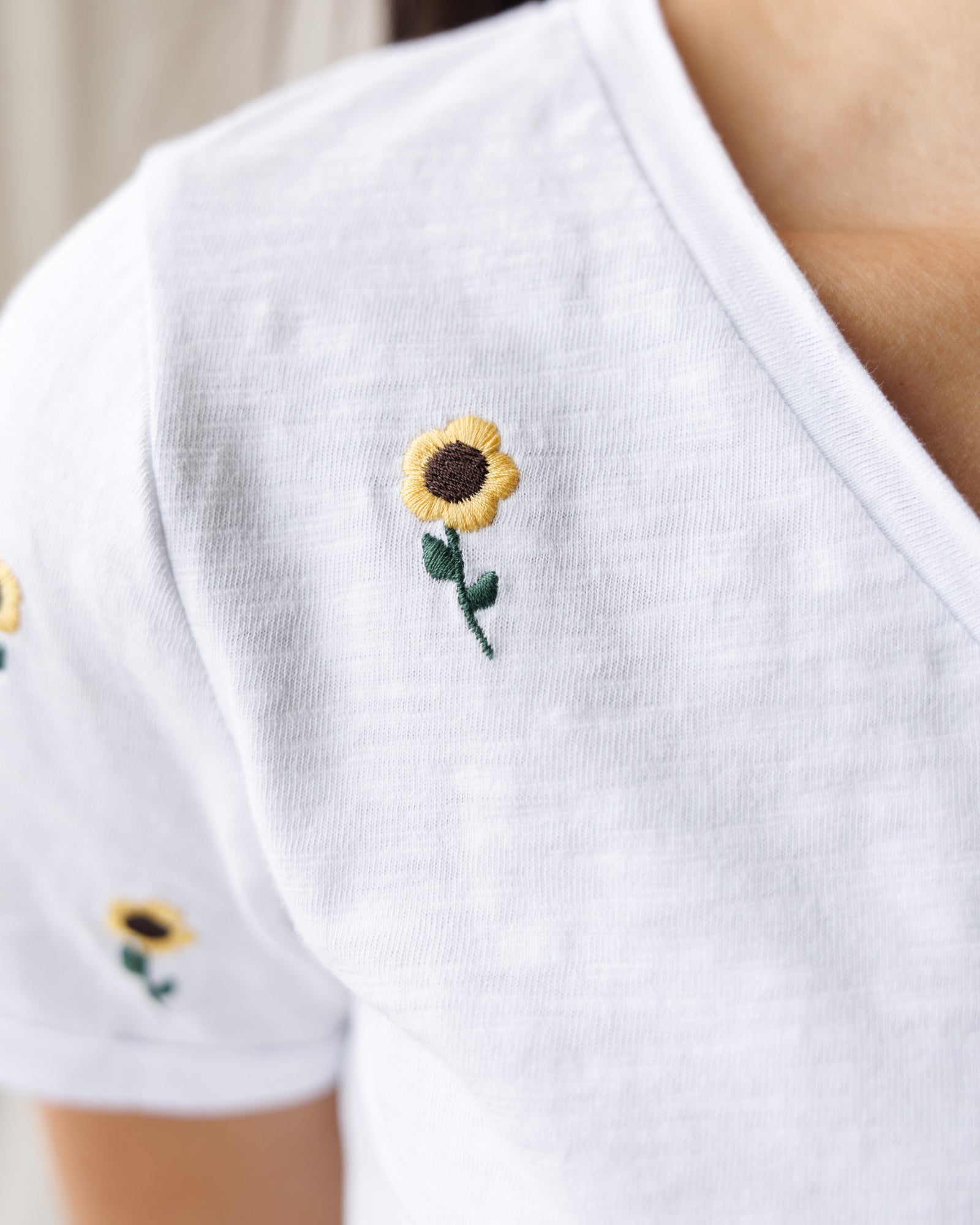 White shirt with embroidered sunflowers on a plain background