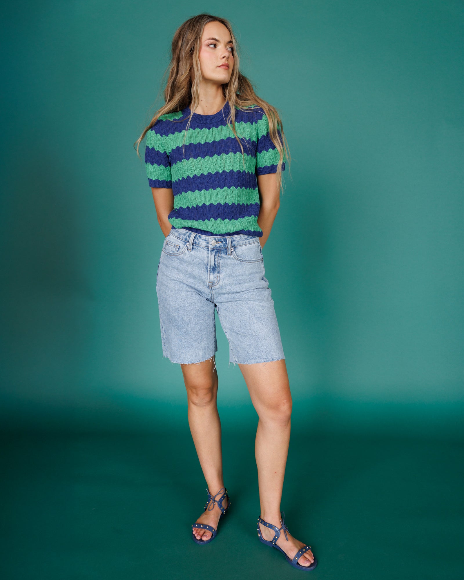 Woman wearing a striped shirt and denim shorts against a teal background