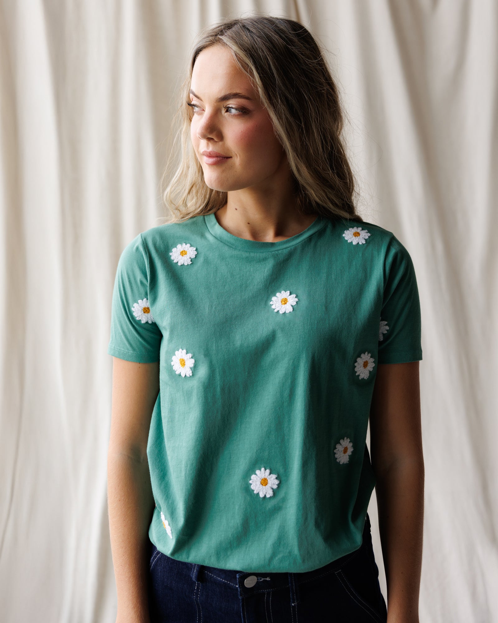 Woman wearing a green t-shirt with white daisy flowers on a plain background