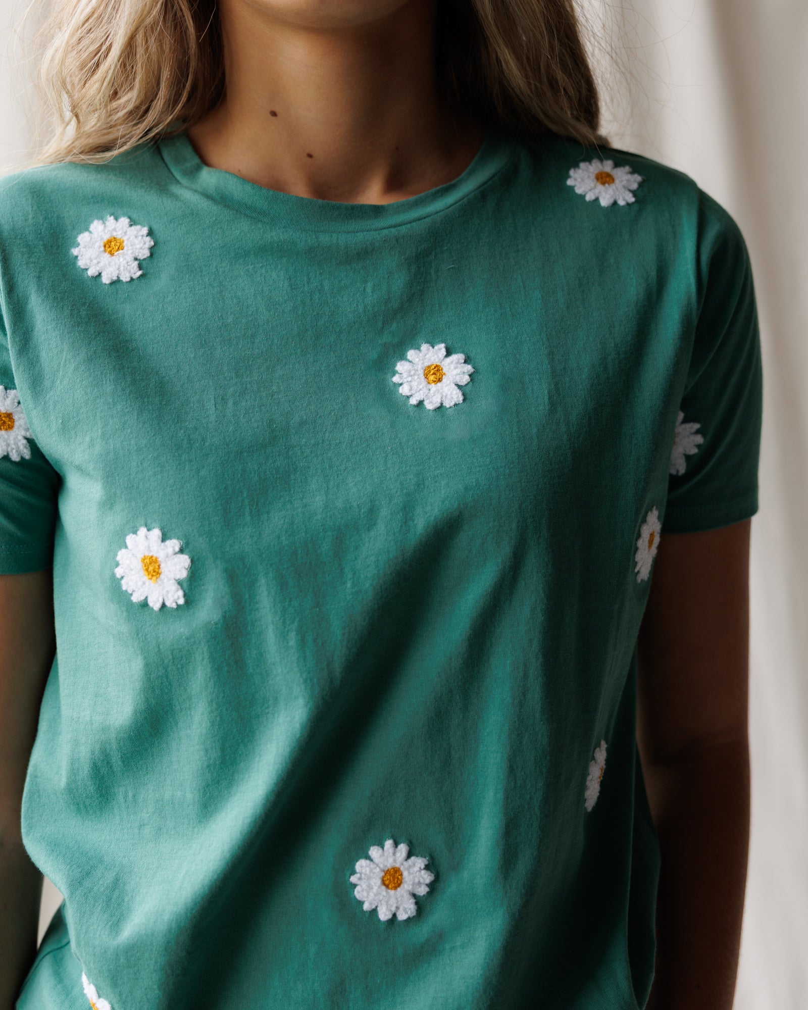 Green t-shirt with white daisy flowers on a neutral background