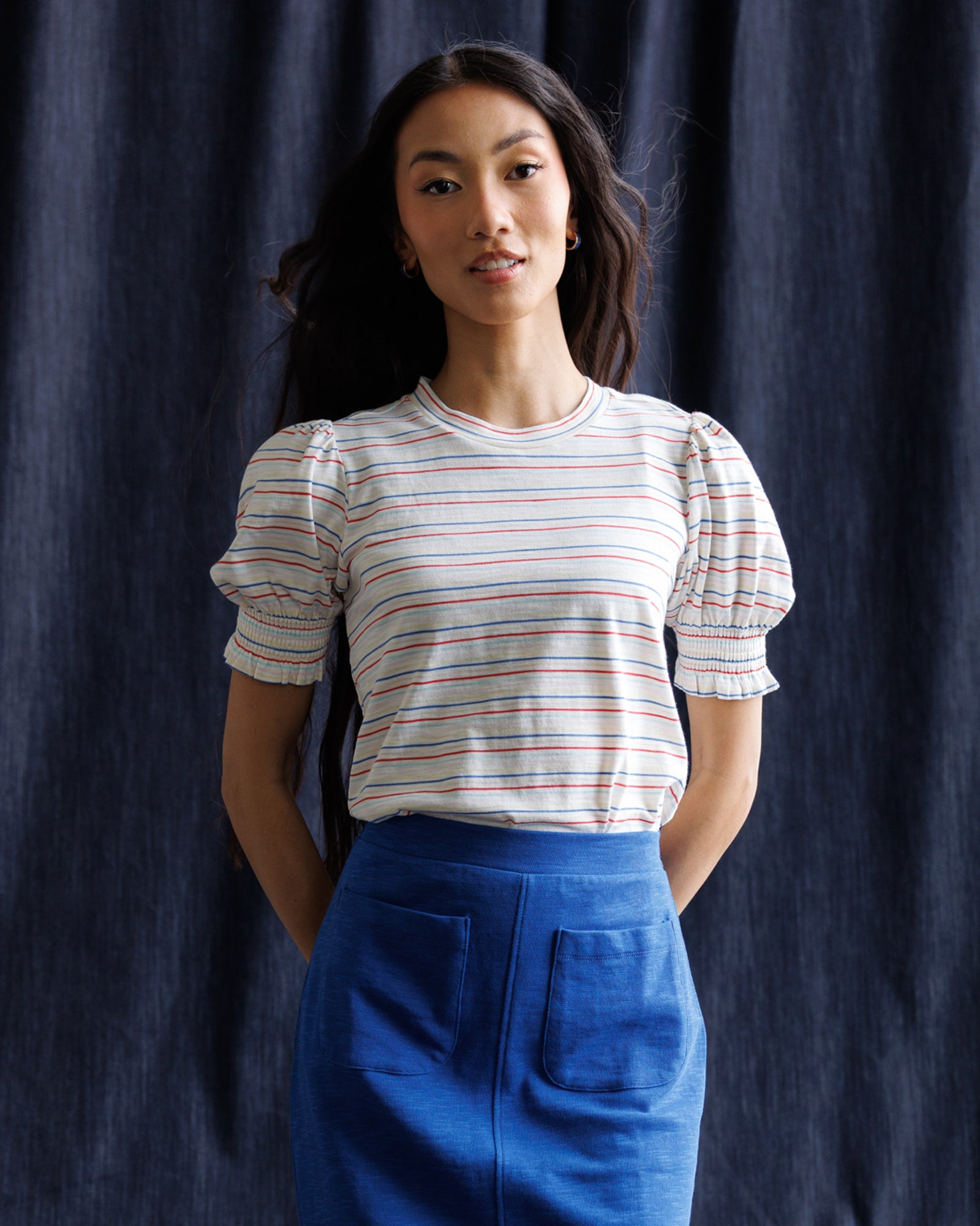 Woman wearing a striped shirt and blue skirt against a navy background