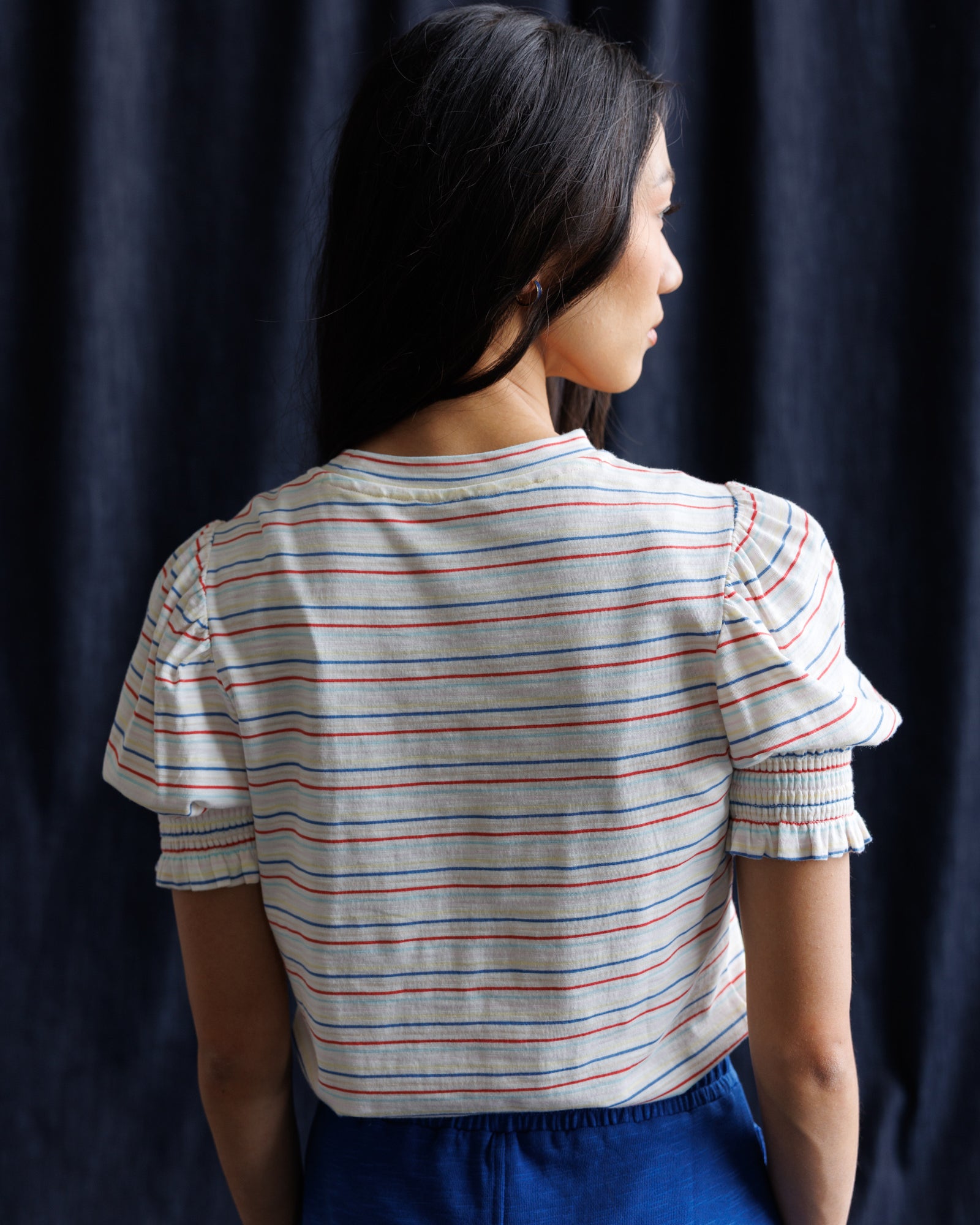 Woman wearing a striped shirt and blue skirt against a navy background