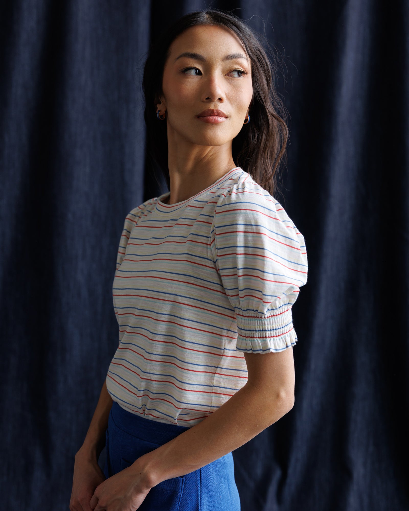 Woman wearing a striped shirt and blue skirt against a navy background
