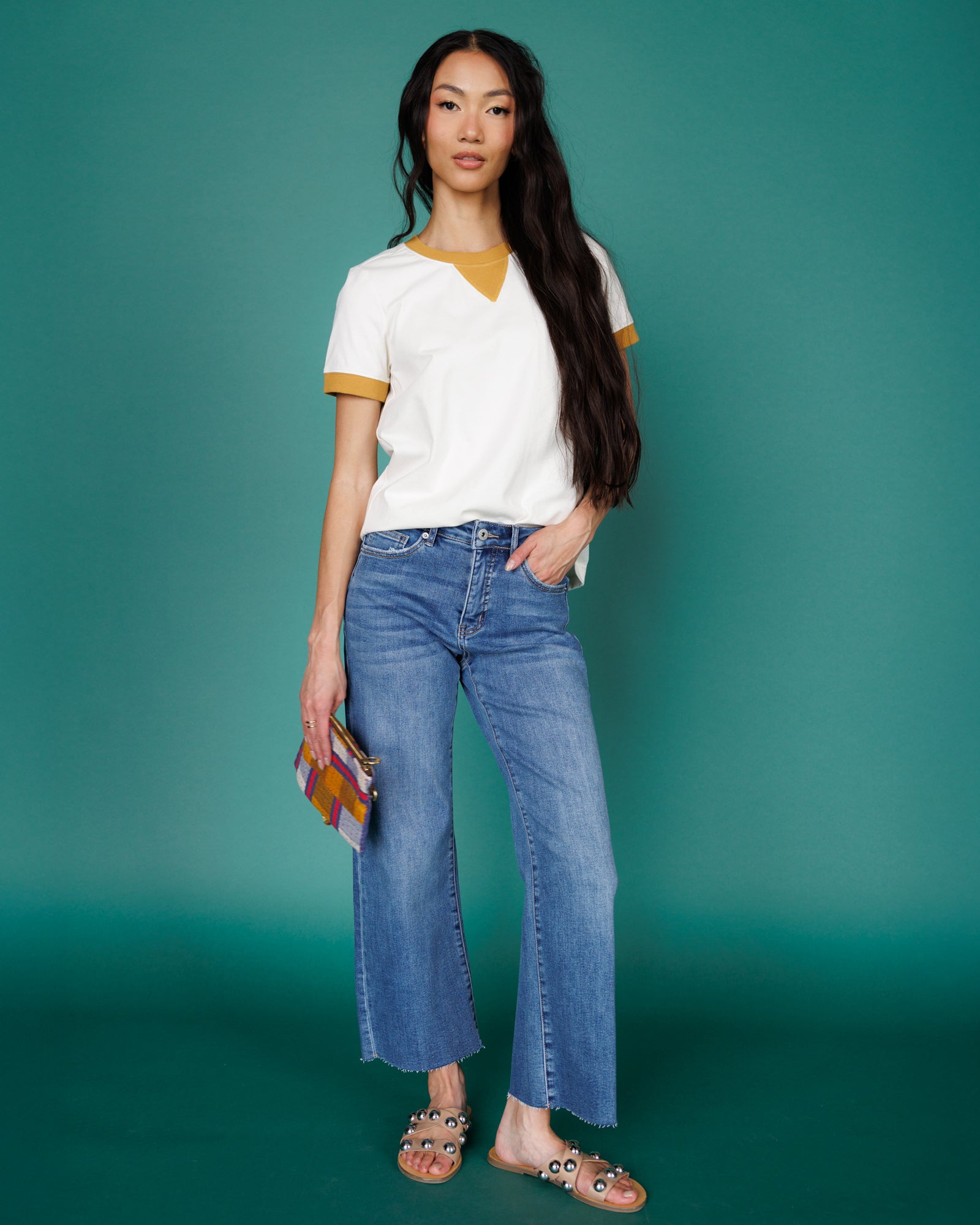 Woman wearing a white shirt with yellow trim and blue jeans against a teal background