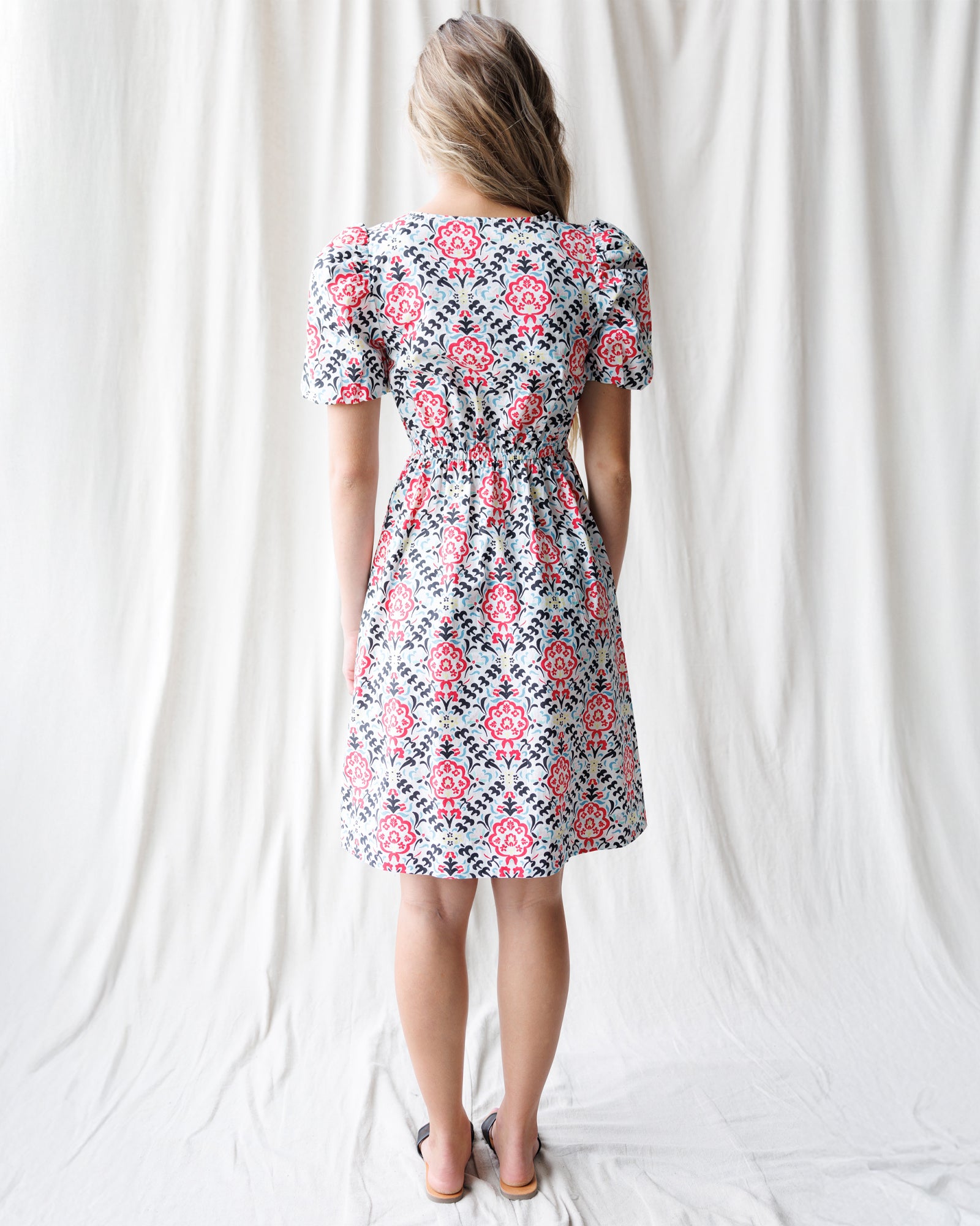 Woman wearing a floral dress standing against a white curtain