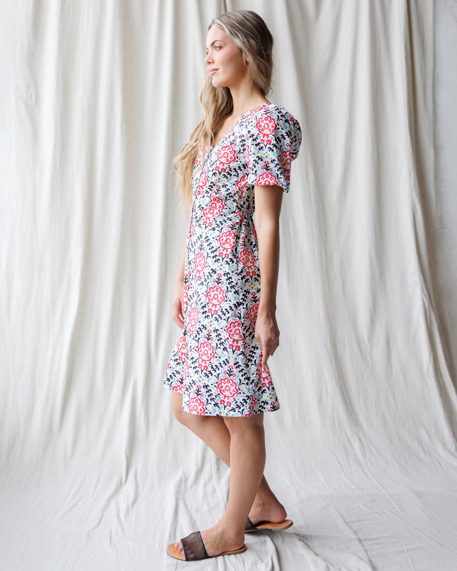 Woman wearing a floral dress standing against a white curtain.