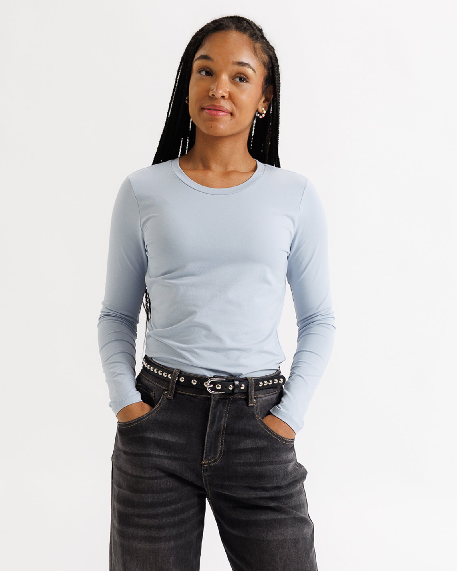 Woman wearing a light blue long-sleeve top and dark jeans on a white background
