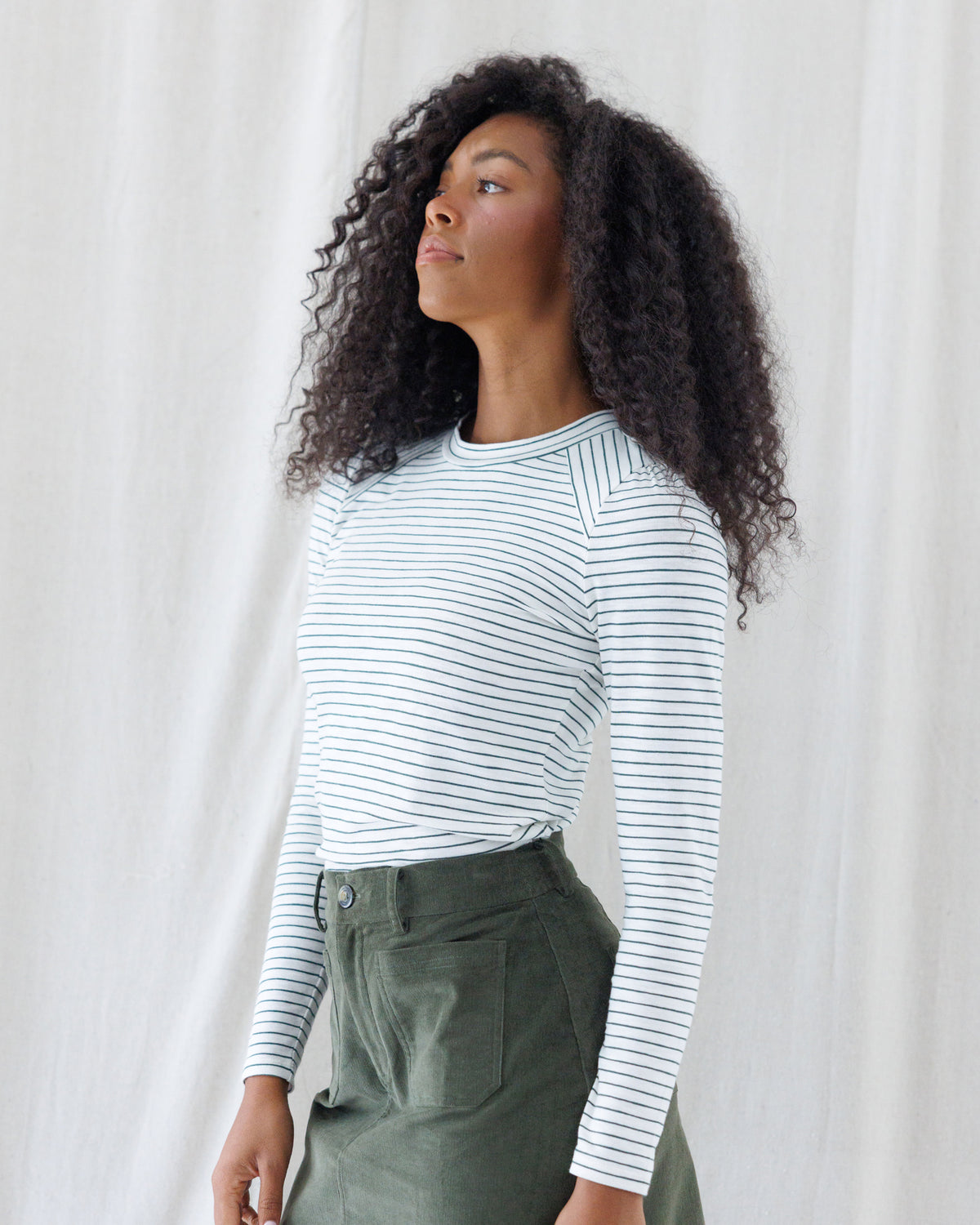 Angled front view highlighting the close, tailored fit of the white and navy striped long-sleeve shirt, featuring set-in angled shoulder seams and a banded crewneck.