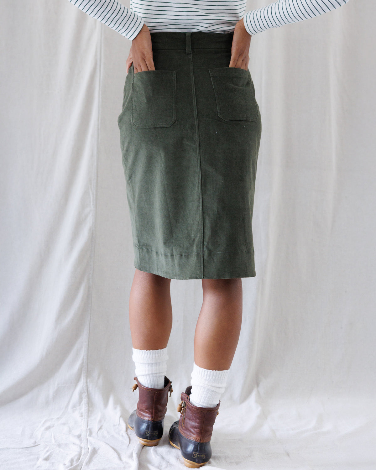 Back view highlighting the straight, tailored silhouette of the olive corduroy skirt with dual back patch pockets and a center back seam.