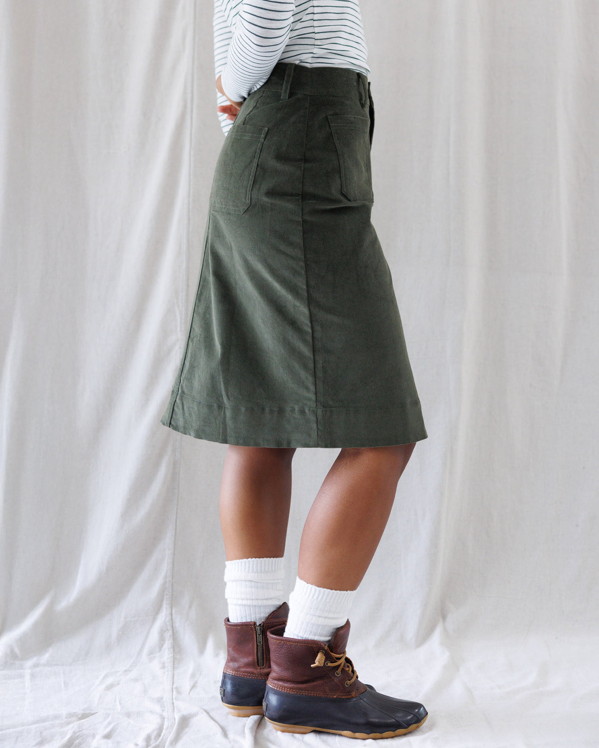 Side profile showing the clean A-line pencil fit, structured waistband, and knee-skimming straight hemline of the olive corduroy skirt.