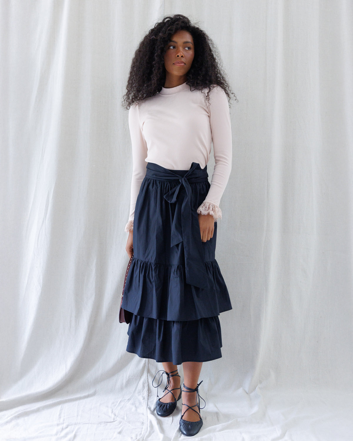 Front view showing the mid-calf silhouette of the black tiered midi skirt with a wide matching waist tie knotted at the front, paired with a tucked-in ribbed top.