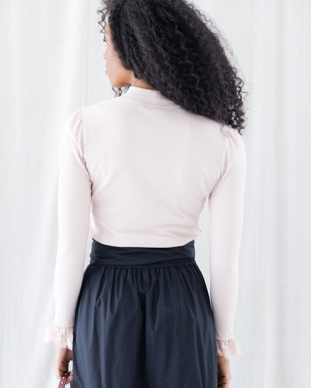 Back view highlighting the seamless fitted cut, clean ribbed texture, subtle shoulder gathering, and high mock neckline of the pale pink long-sleeve shirt