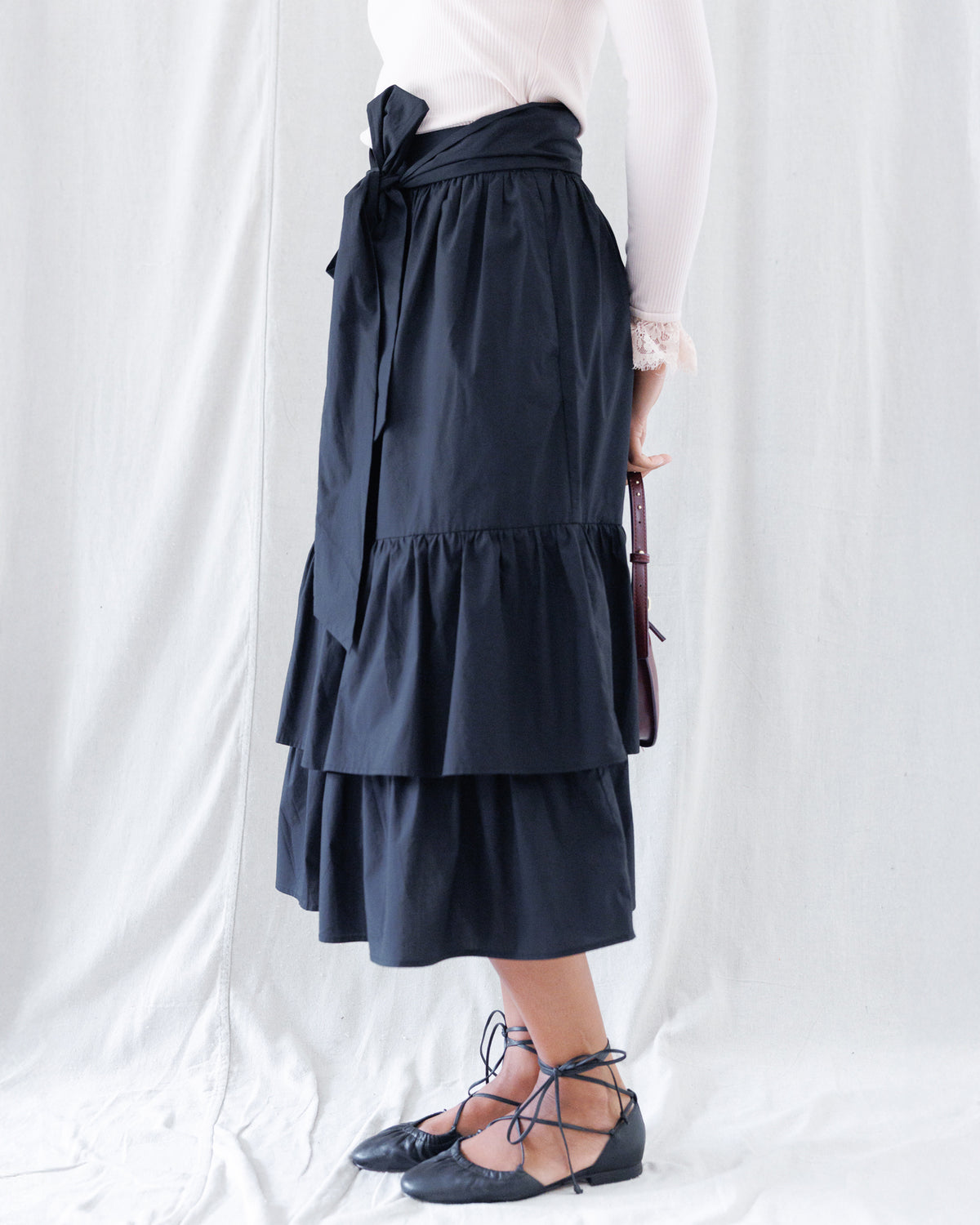 Side profile highlighting the high-rise paperbag-style waistband, statement front sash, and voluminous cascading tiers falling to midi length.