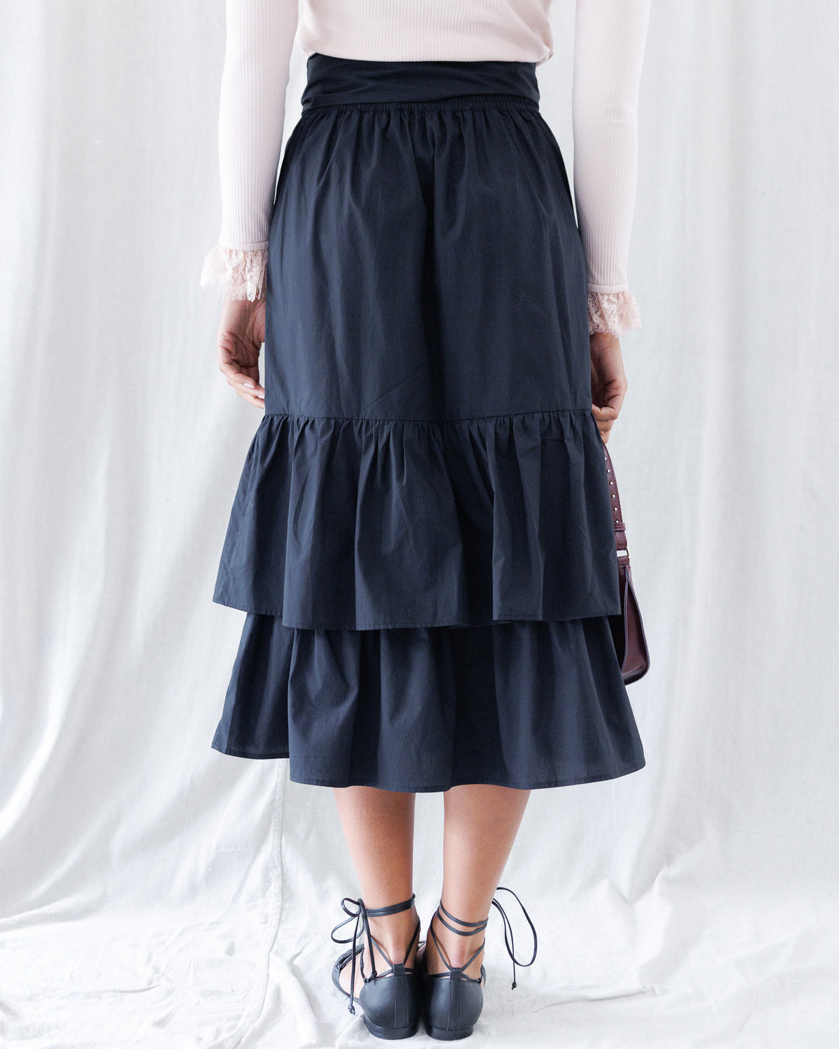 Back view displaying the gathered elastic waistband for flexible fit and the clean drape of the wide two-tier ruffled midi hemline.