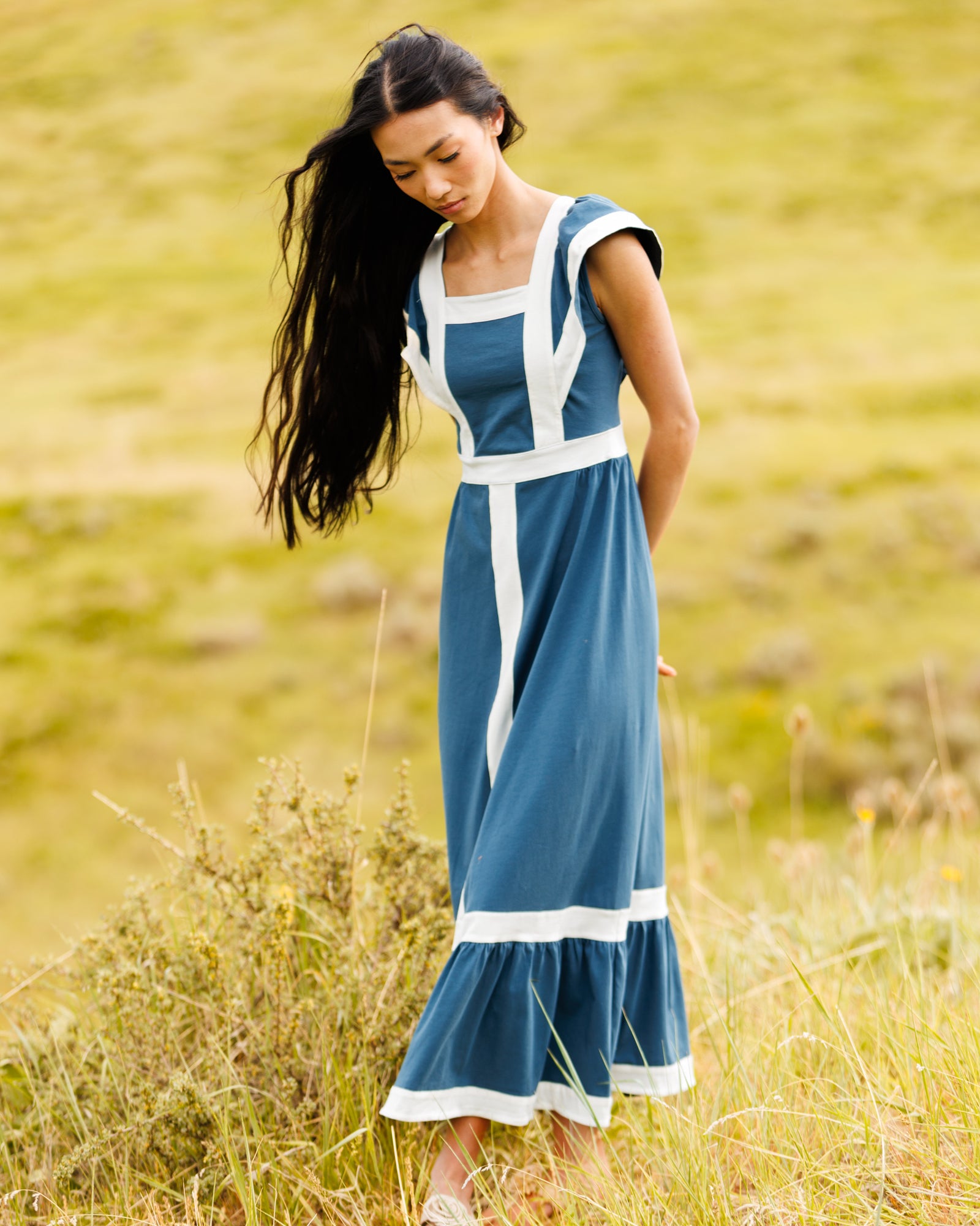 Image of woman wearing a teal and white colorblocked maxi dress standing in a field