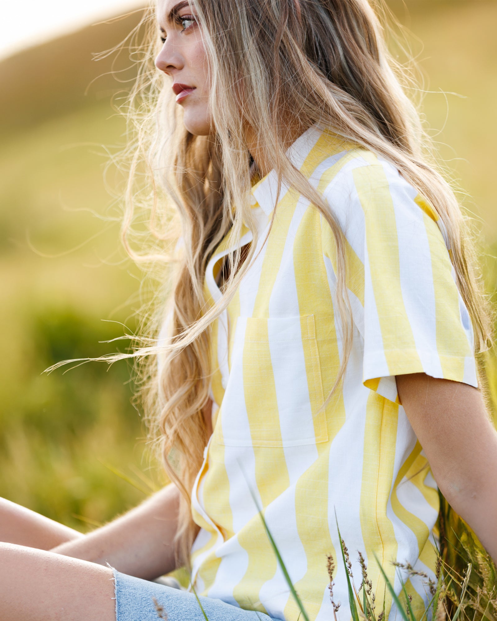 Woman wearing a yellow and white striped top sitting in a field