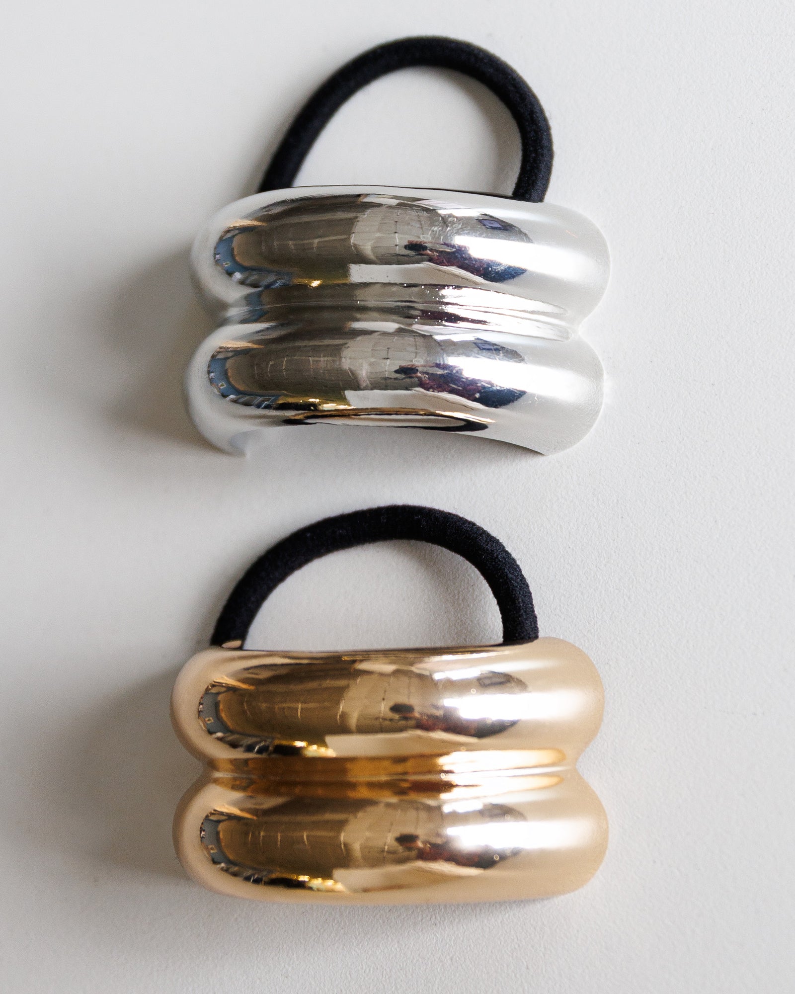 Two metallic hair ties, one silver and one gold, on a white background.