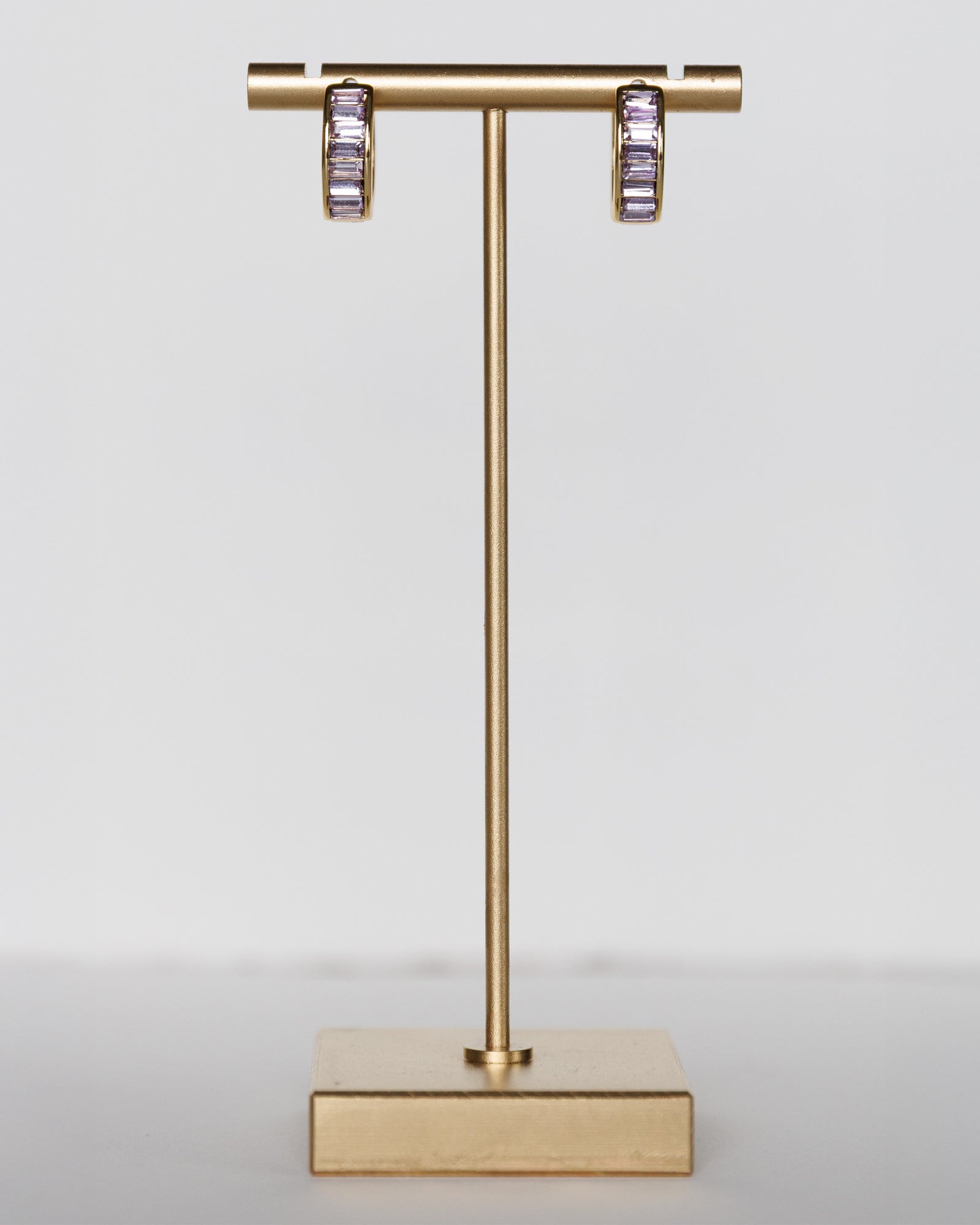 Gold earring stand with hoop earrings on a light gray background