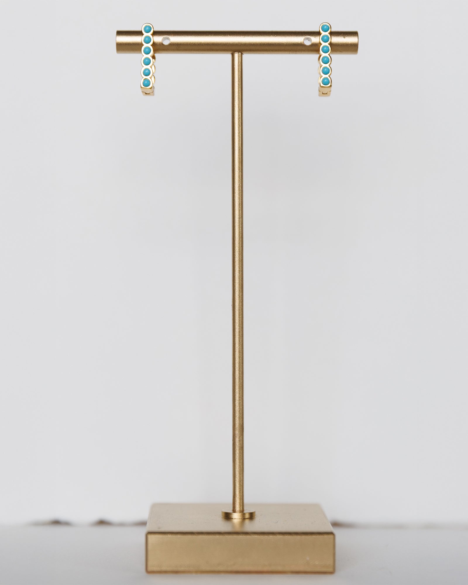 Gold T-shaped earring stand with turquoise earrings on a light gray background