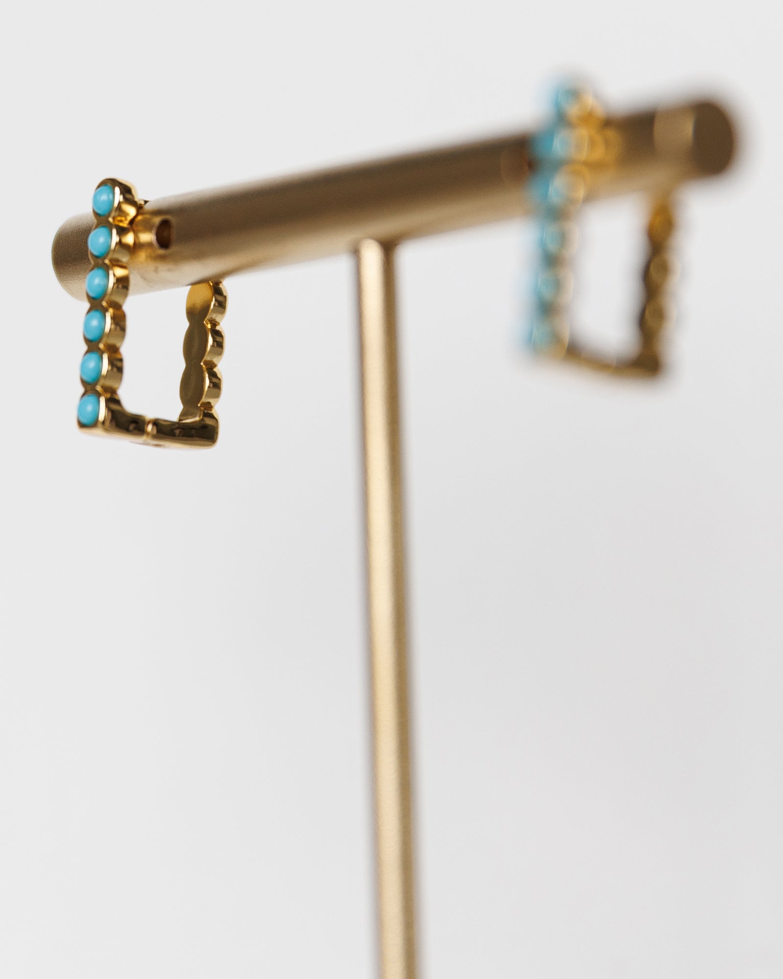 Gold earring stand with turquoise stones on a white background