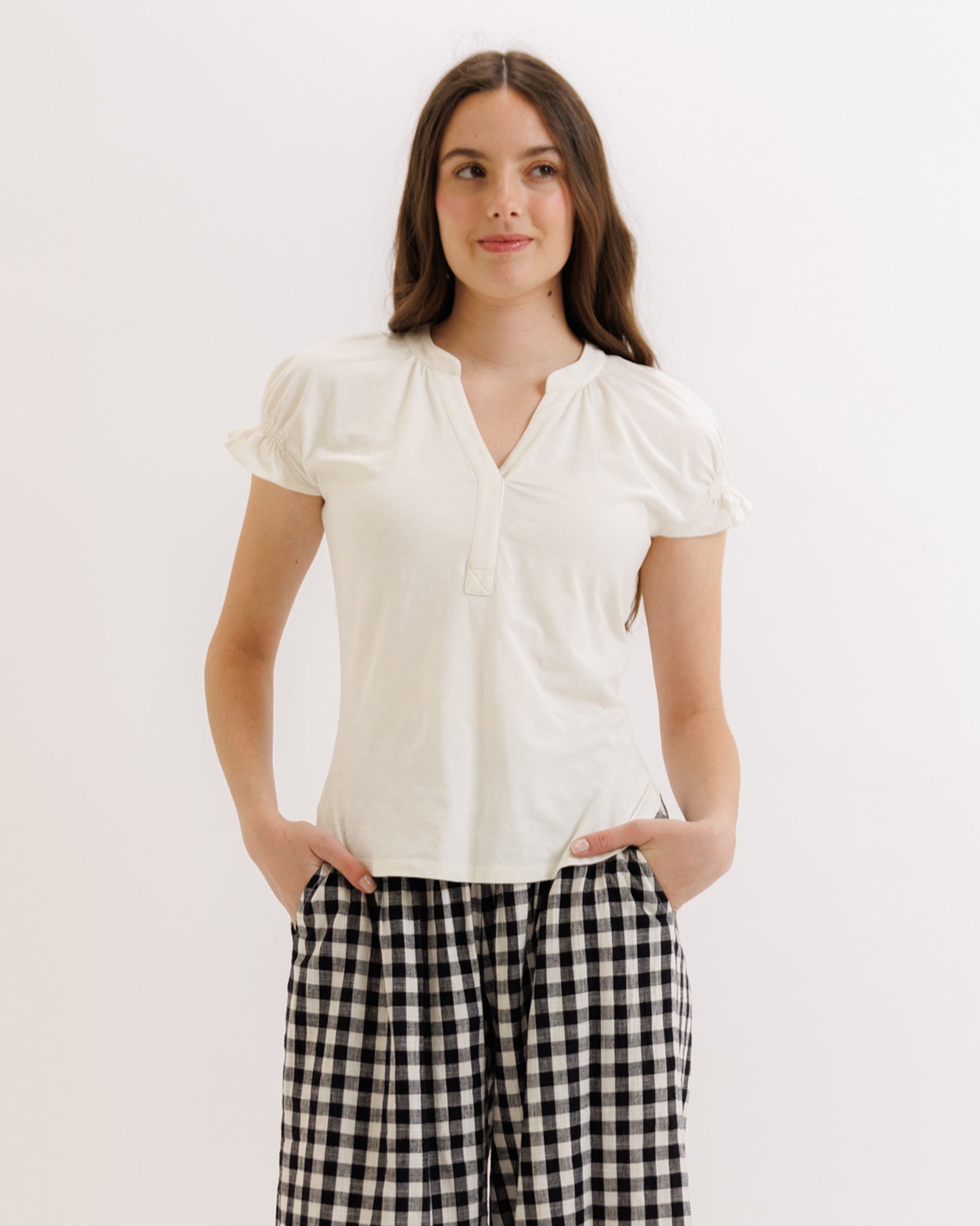 Woman wearing a white blouse and black checkered pants on a light background