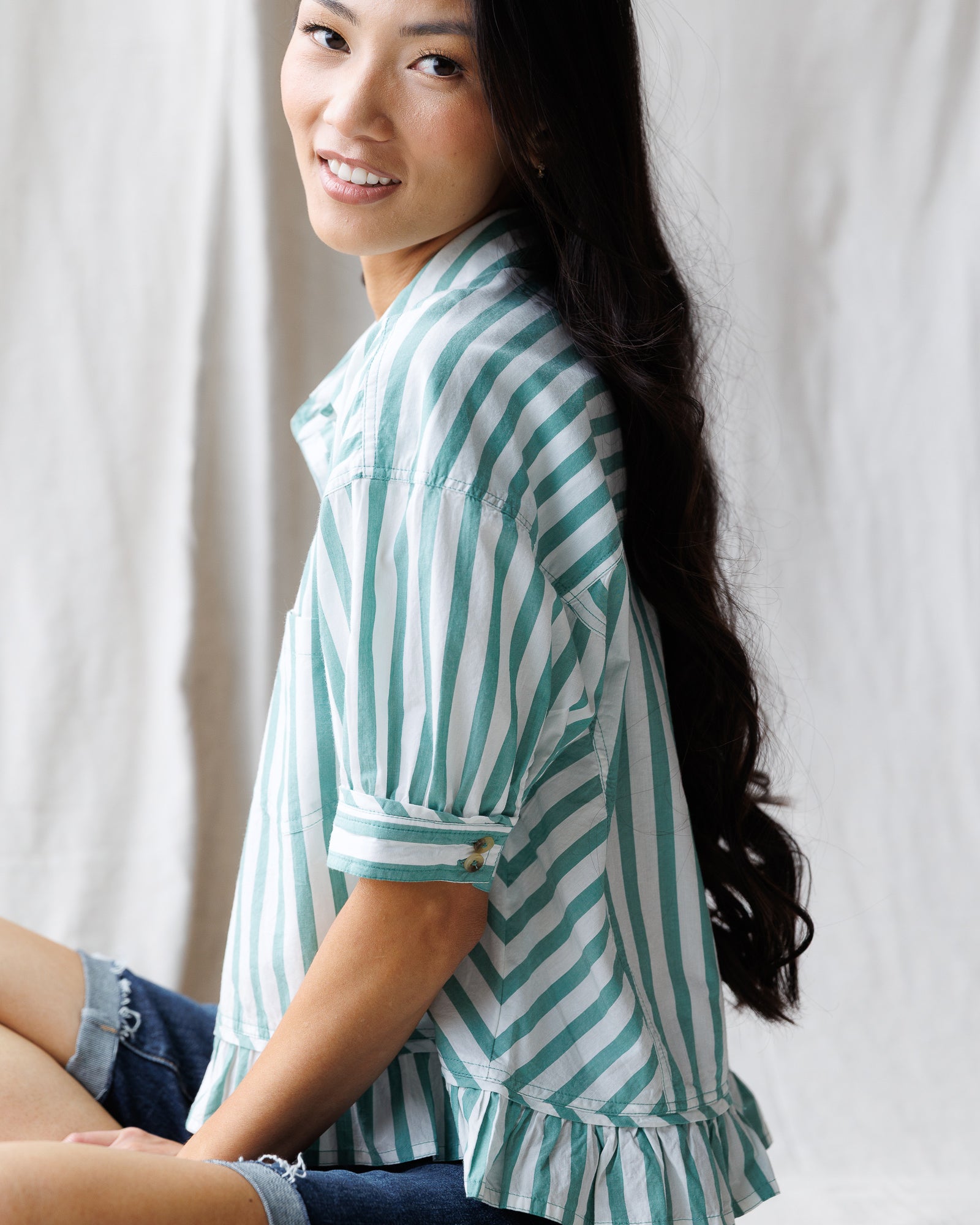 Woman wearing a green and white striped shirt sitting against a plain background