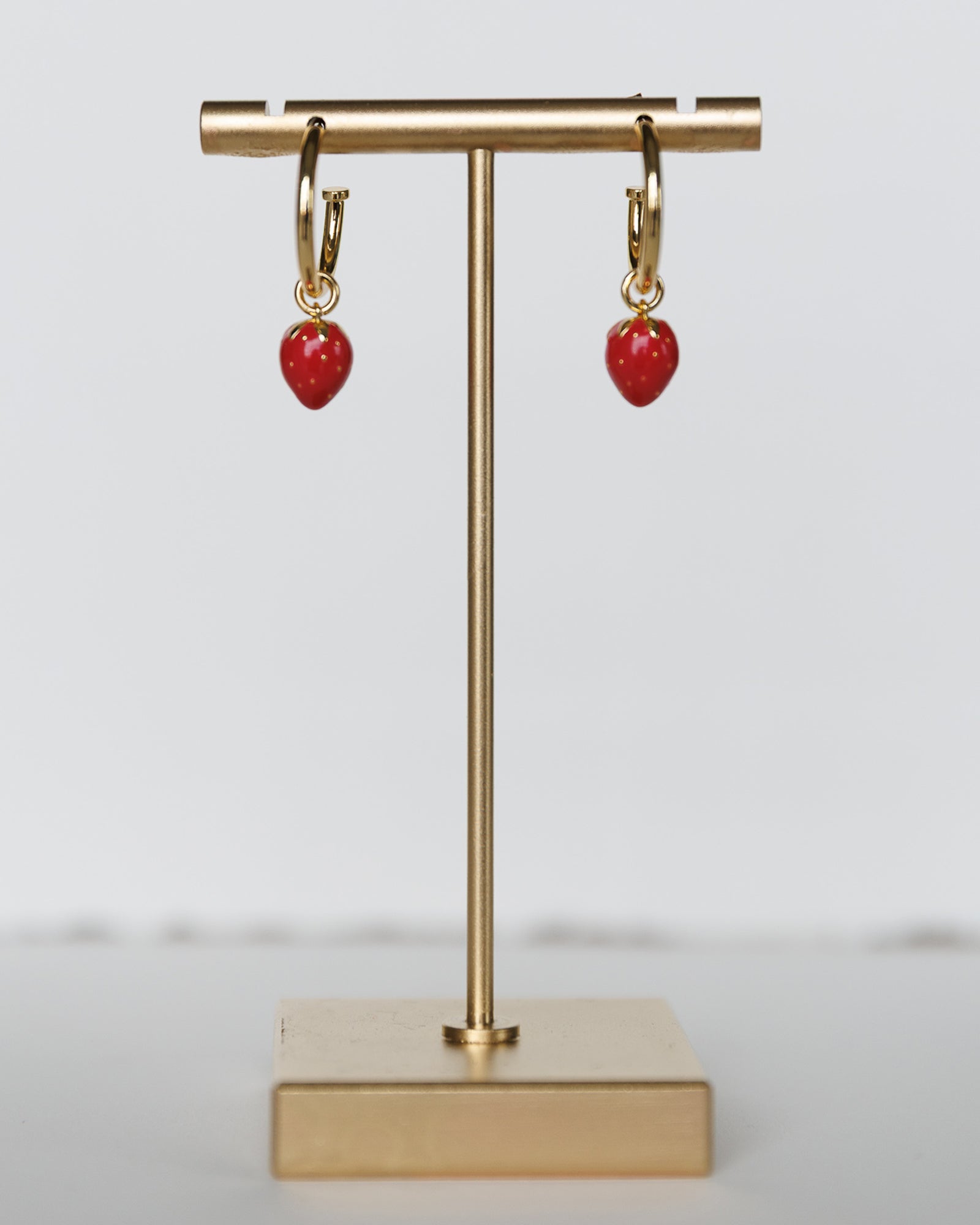 Gold hoop earrings with red coral drops on a gold stand against a light gray background